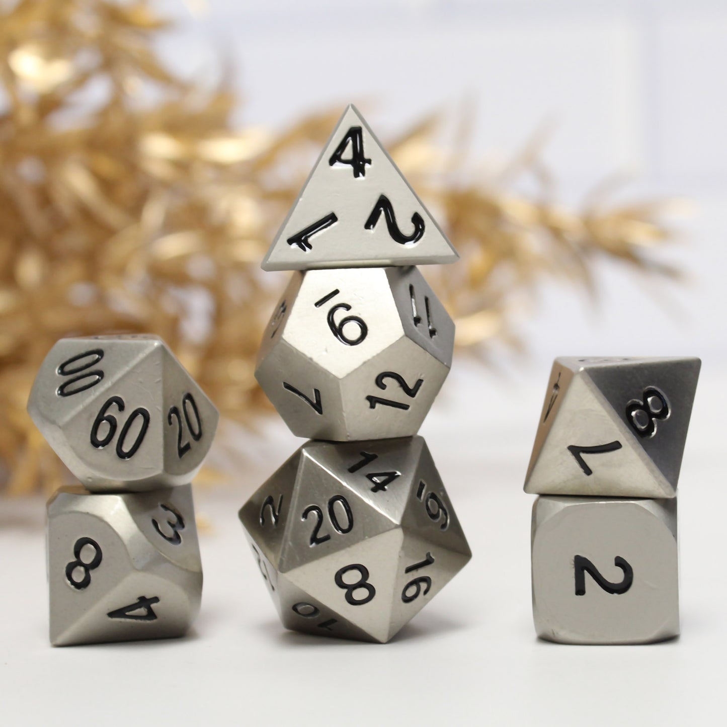 Bright silver dice set arranged in three stacks on a white background with gold foliage behind them