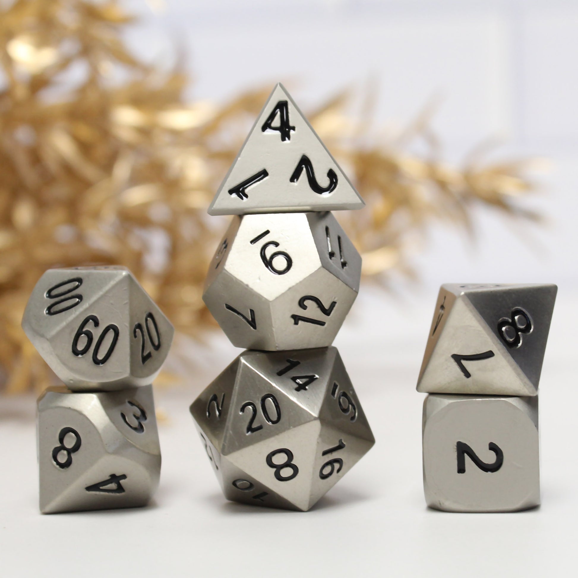 Bright silver dice set arranged in three stacks on a white background with gold foliage behind them