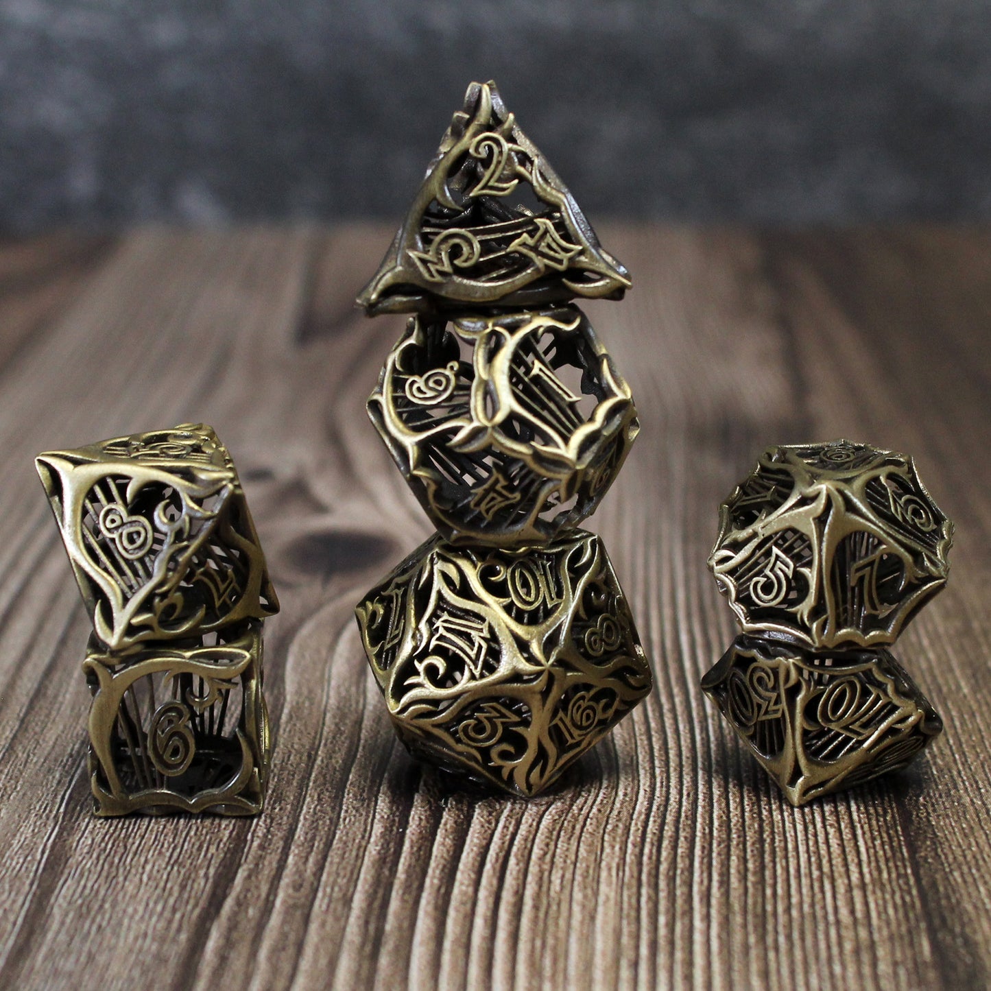 Stacked set of seven bronze bard-inspired hollow metal RPG dice with uninked numbers on a wooden background