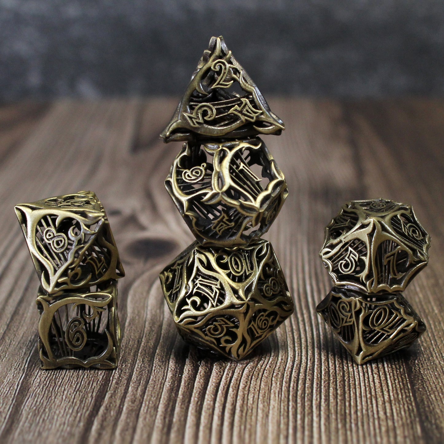 Stacked set of seven bronze bard-inspired hollow metal RPG dice with uninked numbers on a wooden background
