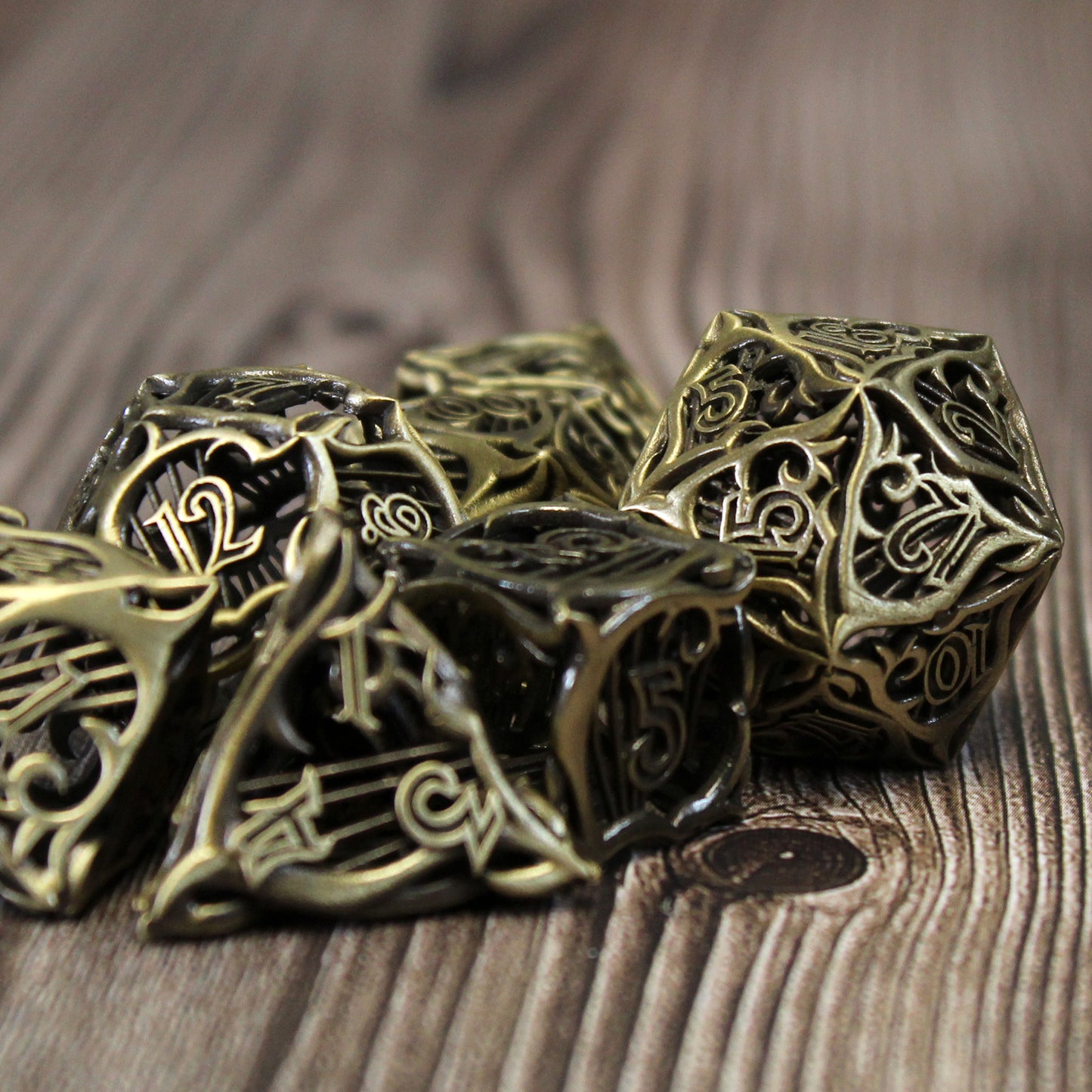 Closeup of a set of seven bronze bard-inspired hollow metal RPG dice with uninked numbers on a wooden background