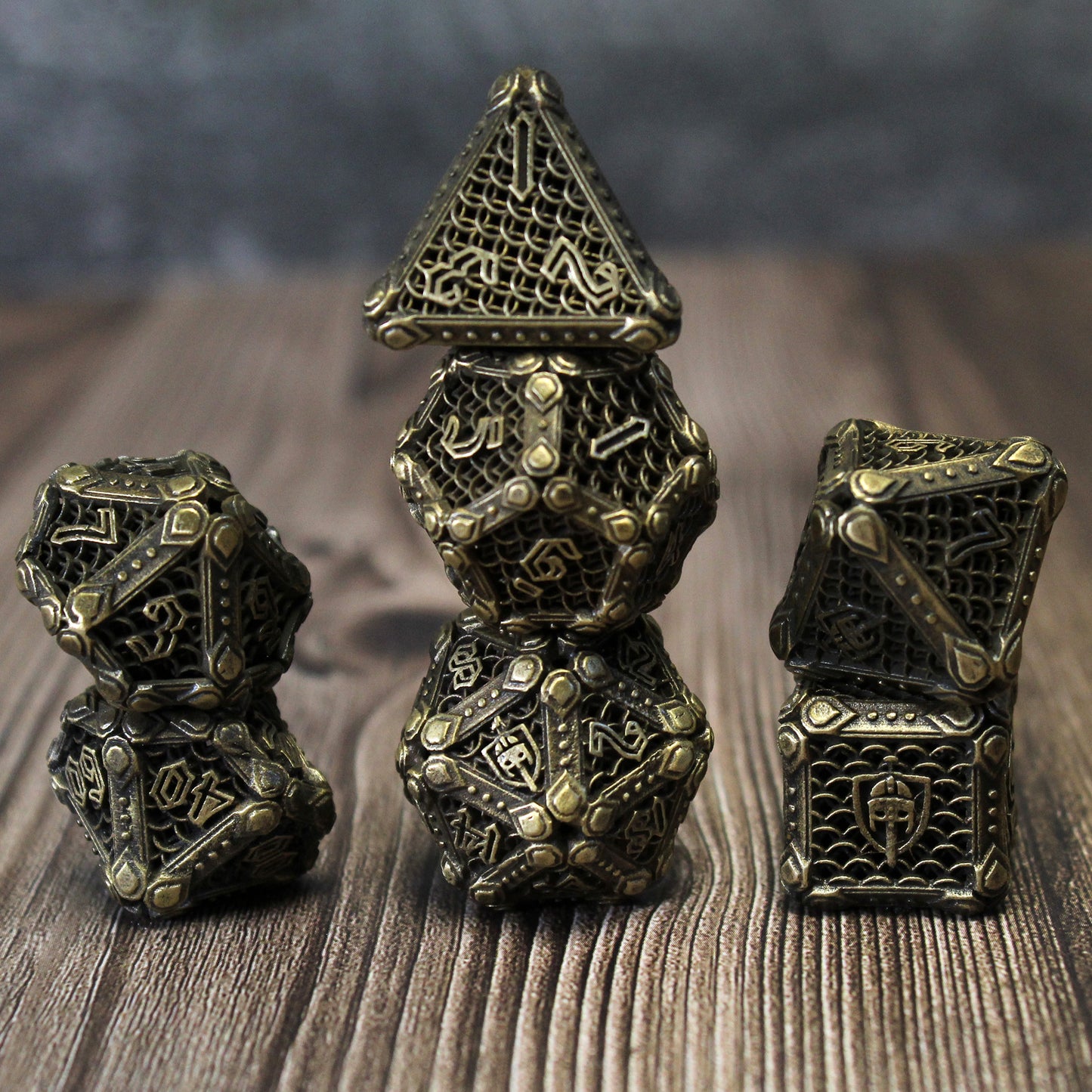 Stacked set of bronze fighter-inspired hollow metal RPG dice with a chain mail background on each die face, uninked numbers, and a helmet, sword, and shield replacing the high number on each die on a wooden surface