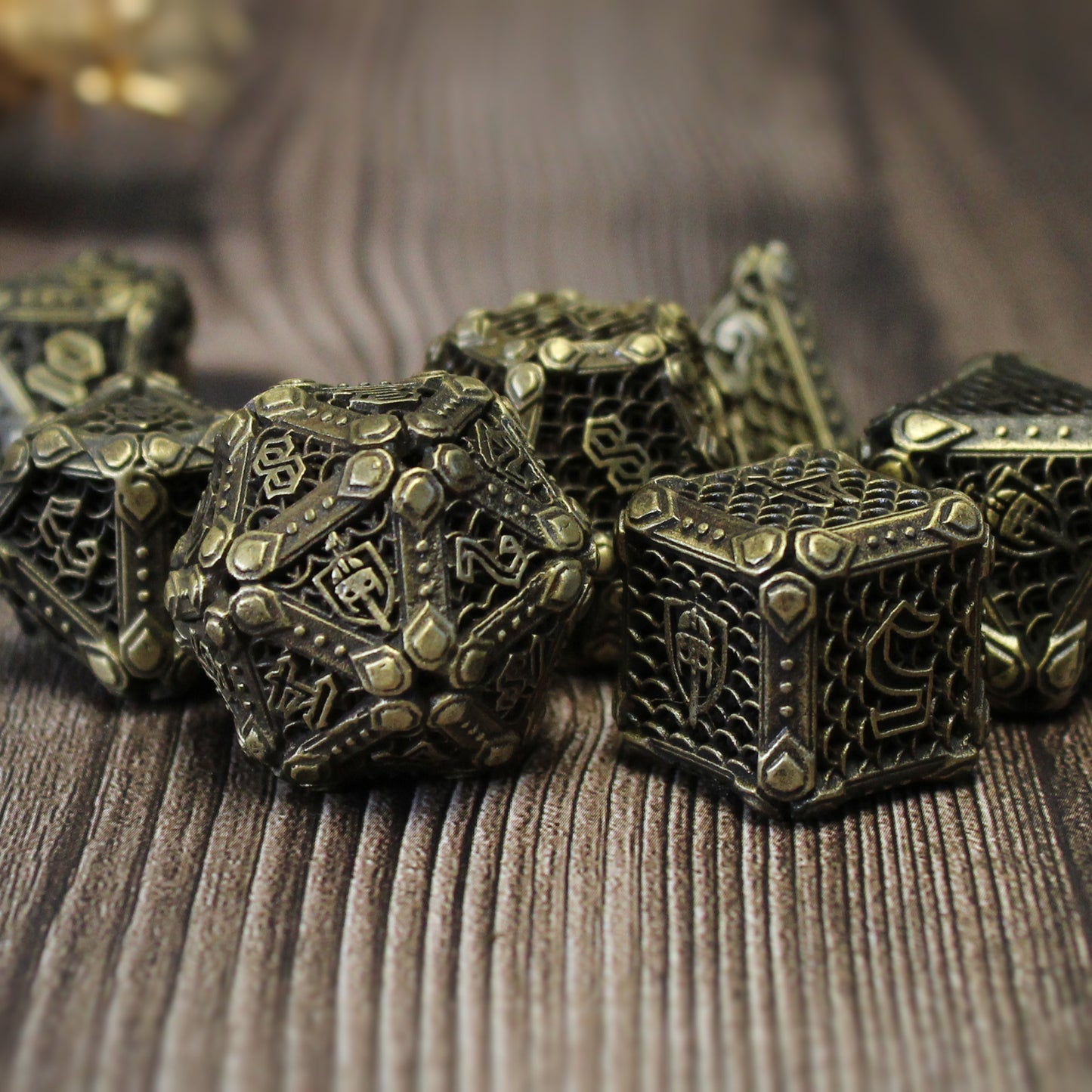 Closeup of a set of bronze fighter-inspired hollow metal RPG dice with a chain mail background on each die face, uninked numbers, and a helmet, sword, and shield replacing the high number on each die on a wooden surface.