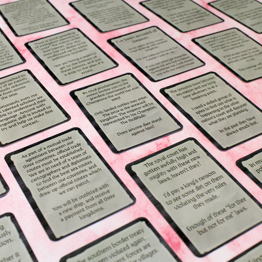 A photo of some example cards from Emissaries & Infiltrators presented as rich paper on a wooden background with the text of the posting in a serif font.
One card reads, "The royal court has gotten awfully high and mighty with these new laws, haven't they?
I'd pay a king's ransom to see some dirt on them violating the very rules they made.
Enough of these 'for thee but not for me' laws."