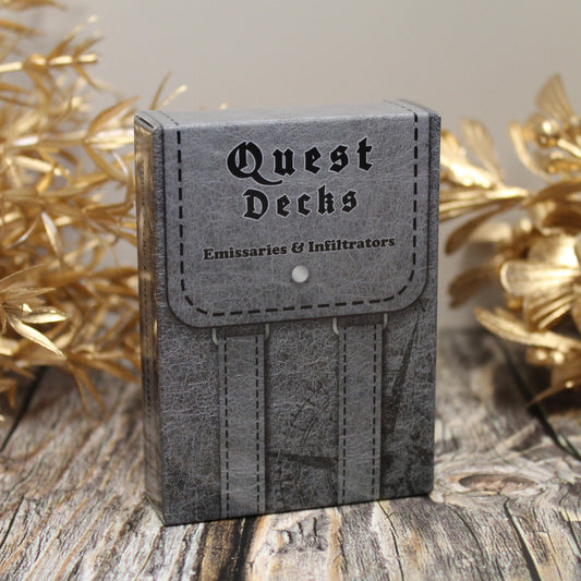 Photo of Quest Deck: Emissaries & Infiltrators physical deck box standing upright on a wooden surface with gold plants behind on a white background.