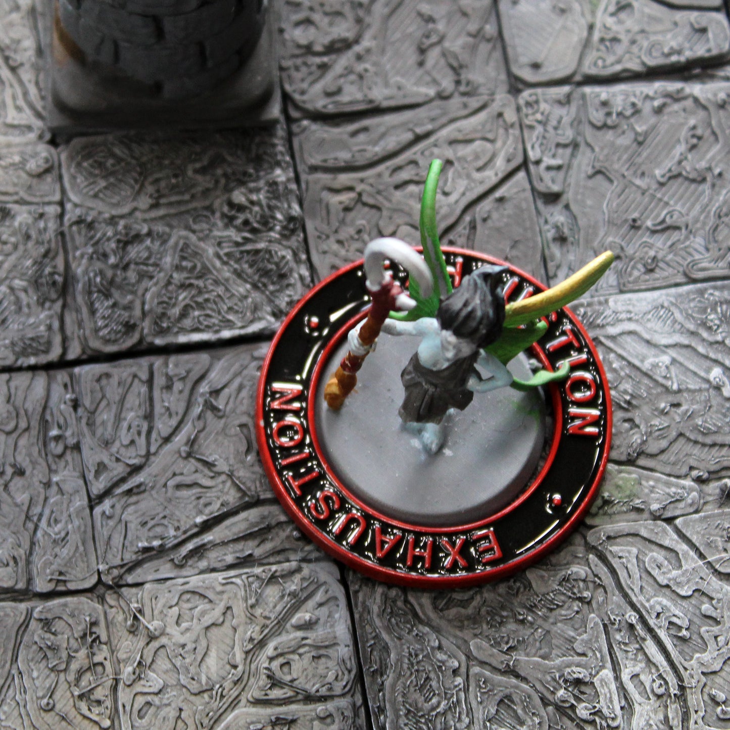 A figure of a winged fairy surrounded by a black ring with a red rim and red text that says "Exhaustion" on it on a gray grid.