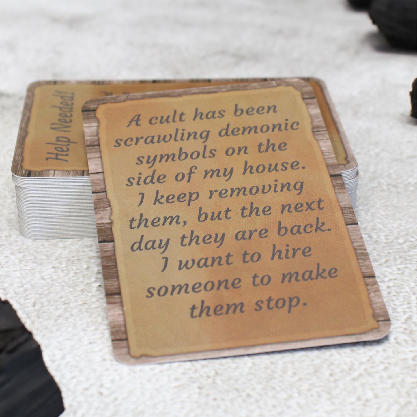 An example card from the Fiendish Missives deck that reads, "A cult has been scrawling demonic symbols on the side of my house. I keep removing them, but the next day they are back. I want to hire someone to make them stop."