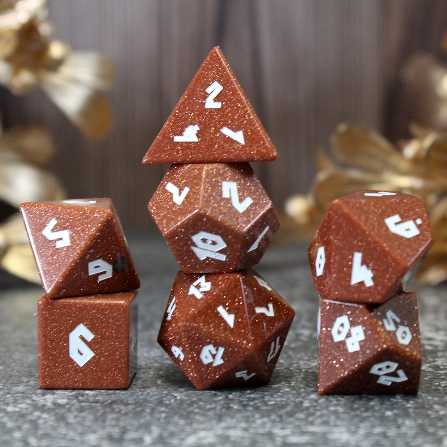 Goldstone dice set arranged in three stacks on a pebble patterned play mat with gold flowers behind them.