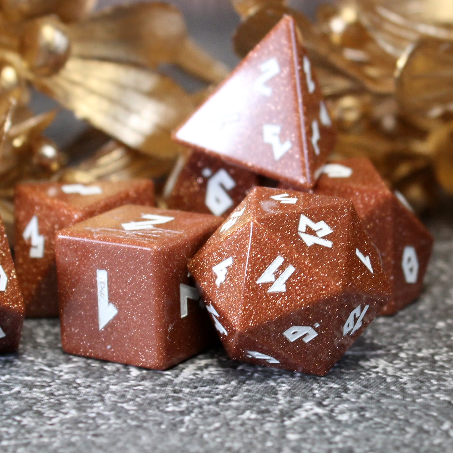 Goldstone dice scattered on a pebble-patterned play mat with gold flowers behind them.