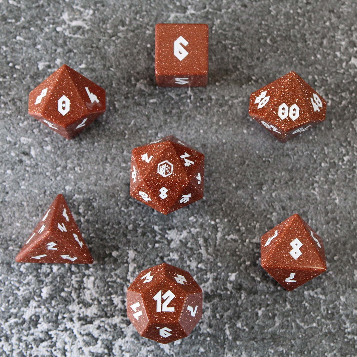 Goldstone dice set arranged in a circle on top of a gray surface. The D20 is in the middle, with the other six dice arranged around it.
