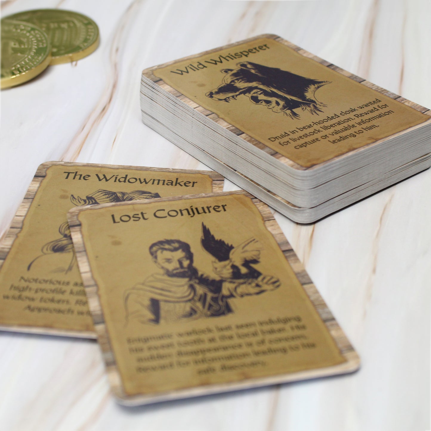 An example card from the Lost & Wanted deck on a white wooden surface with coins around it.
The card reads, "Wild Whisperer" above a side-view portrait of a man with a bear-hooded cloak, below the portrait is the text, "Druid in bear-hooded cloak wanted for livestock liberation. Reward for capture of valuable information leading to him."