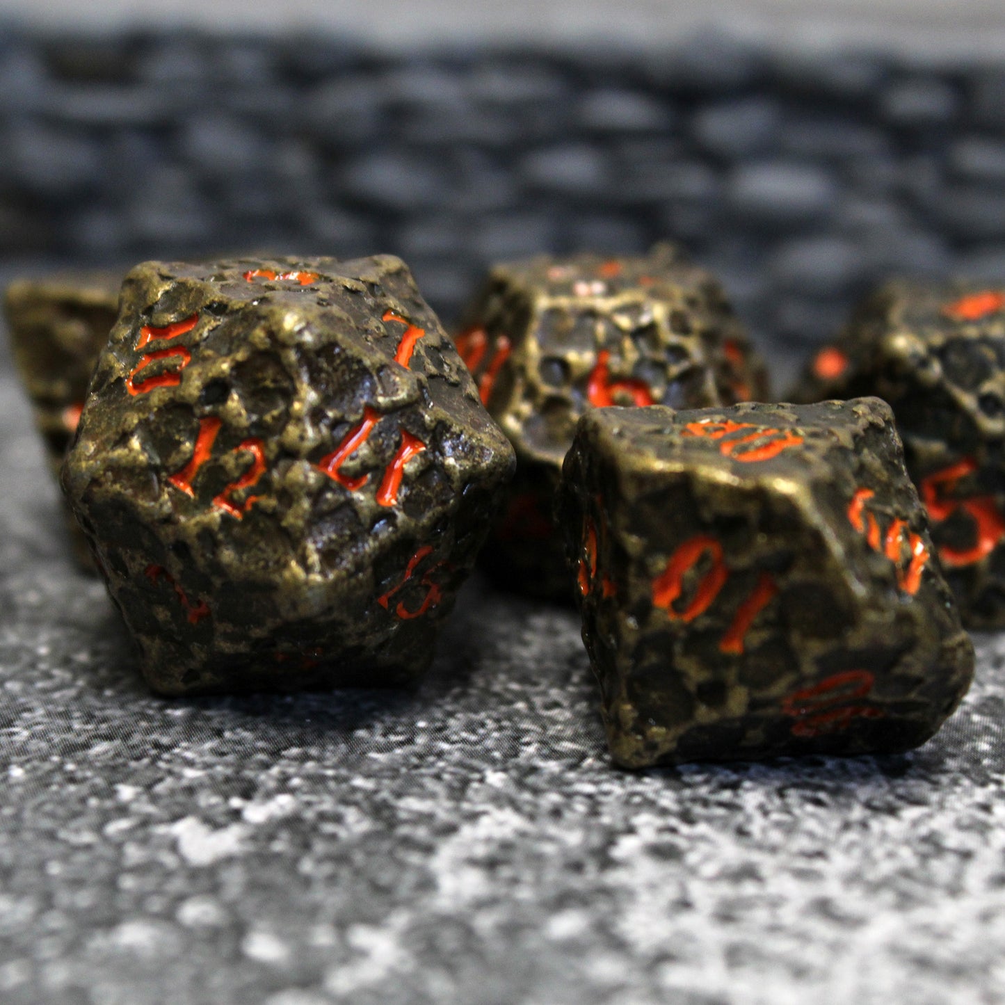 Dice from the Geomancer Black dice set arranged on a stone surface with a miniature wall in the background. The d20 and d10 dice are in the foreground with other dice from the set behind.