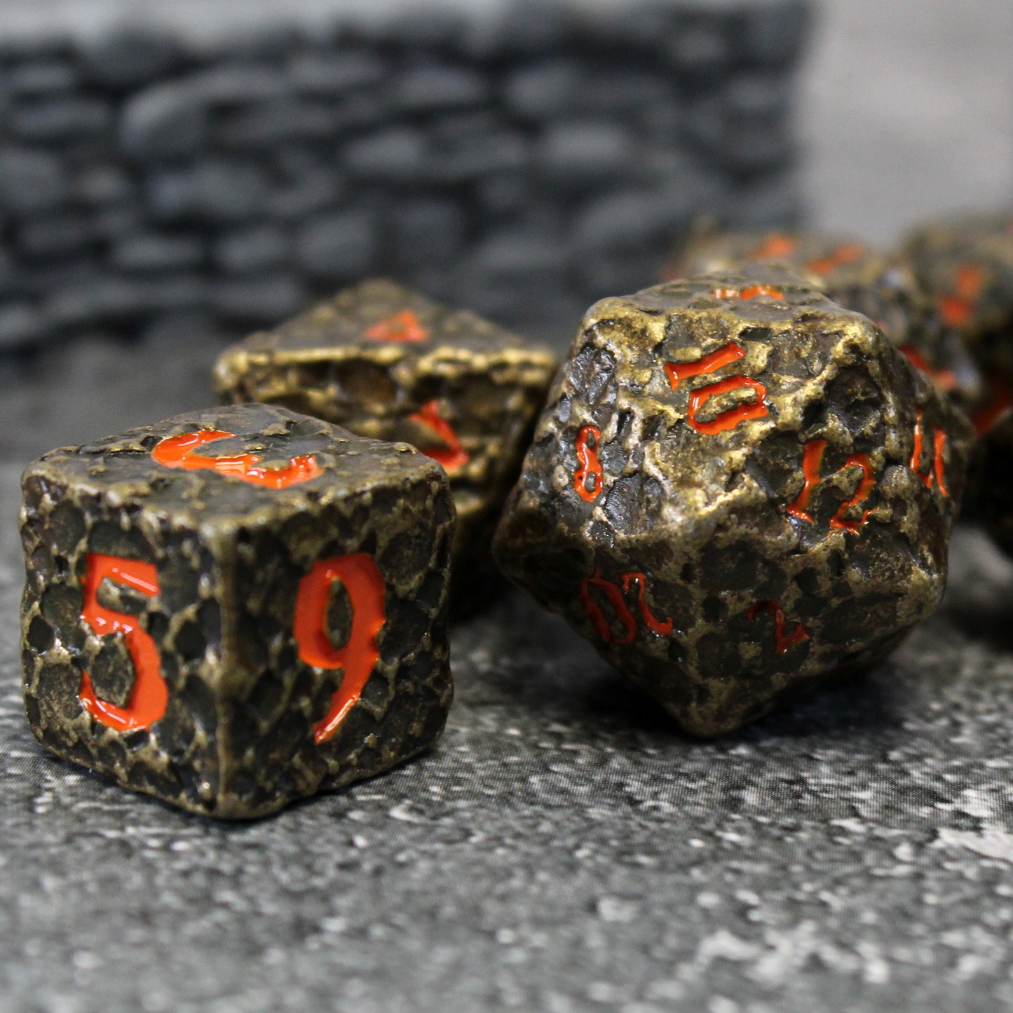 Closeup shot of the Geomancer Black dice on a stone printed cloth with a miniature wall in the background out of focus. Each die has red numbering on a worn black finish.