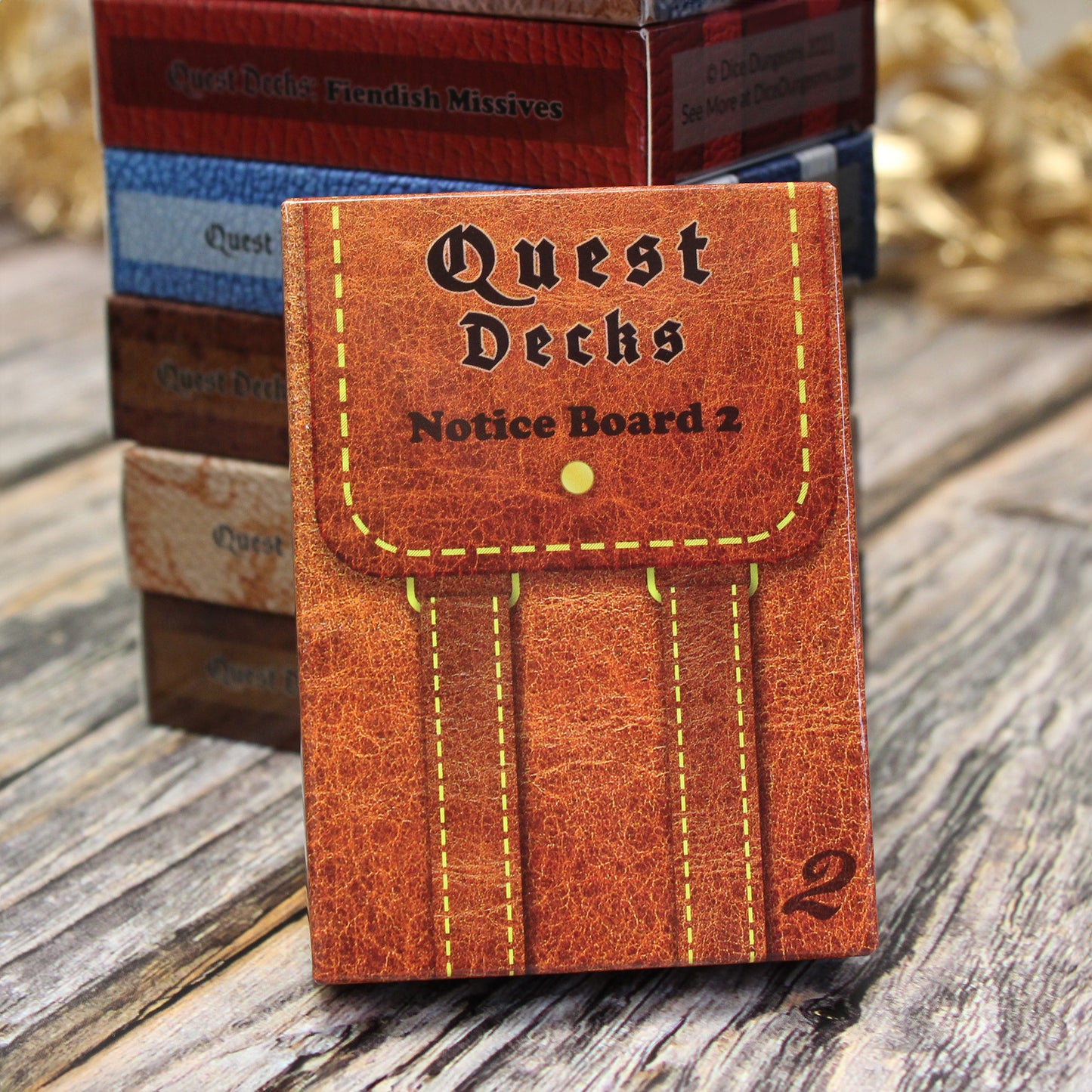 Photo of Quest Deck: Notice Board 2 physical deck box leaning upright on a wooden surface against other Quest Decks. This deck focuses on quest prompts that fit into almost any world.
