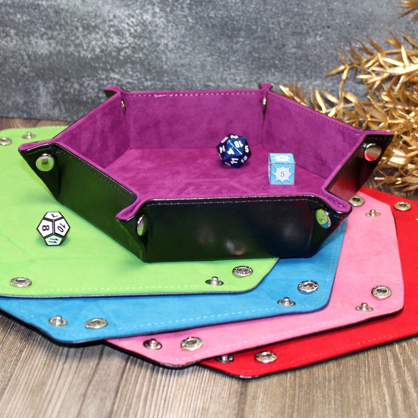 Multiple color options of the Folding Hexagonal Dice Tray arranged at an angle on a wooden surface, highlighting the texture and design from various perspectives.