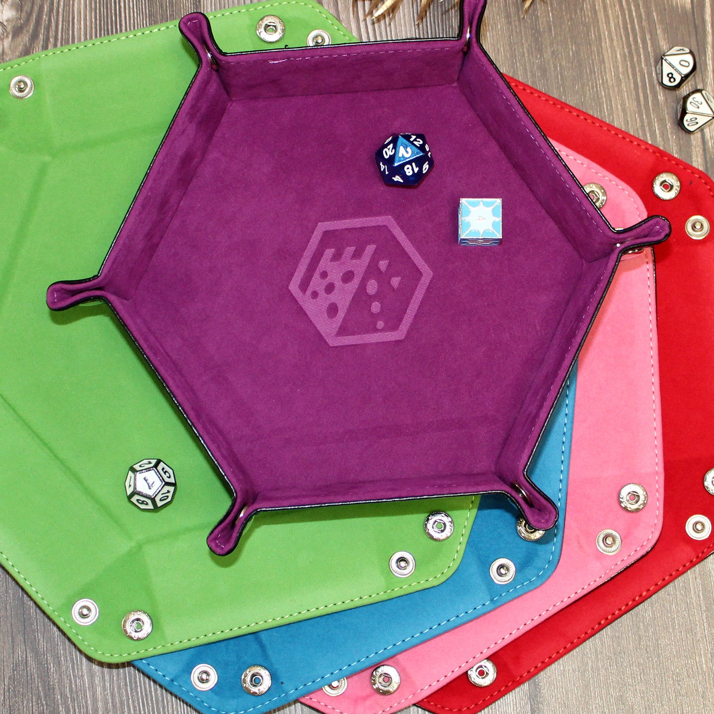 All color options of the Folding Hexagonal Dice Tray displayed on a wooden background, shot from above, with a variety of velvet and PU leather combinations.