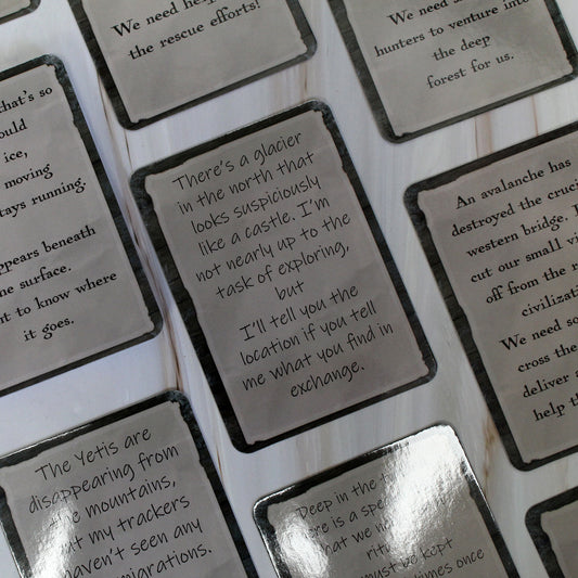 A batch of Snowbound quest cards arranged on a white wood table, displaying various quest prompts related to frozen landscapes and cold-hardened beasts.