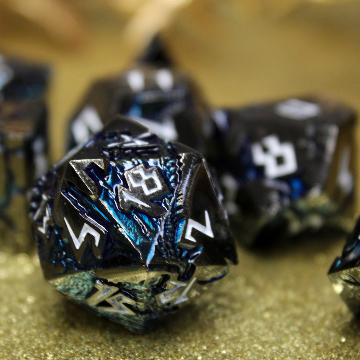 Close-up of Stormrift black nickel D20 with deep blue scars and white numbers, set against a gold background for a striking contrast.