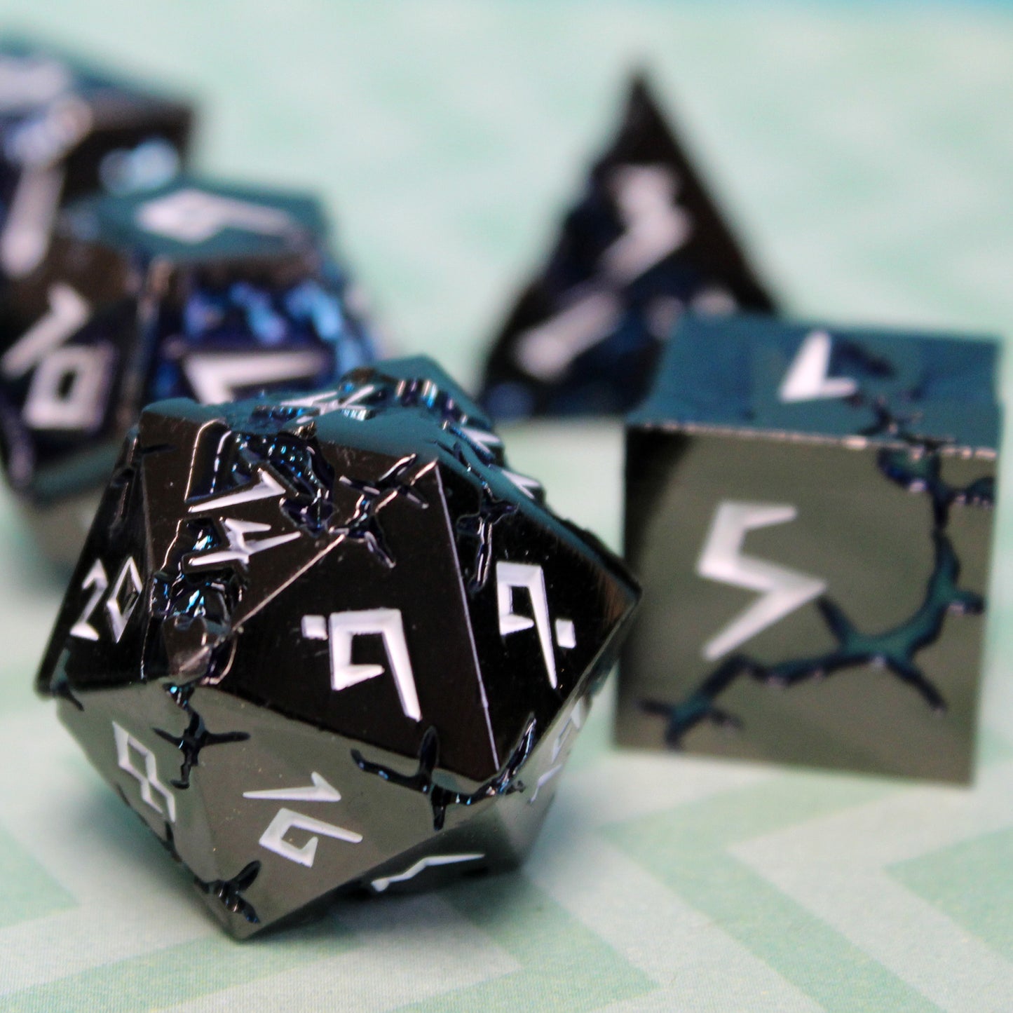 Close-up of Stormrift black nickel D20 and D6 with deep blue scars and white numbers, designed for D&D and fantasy RPGs.