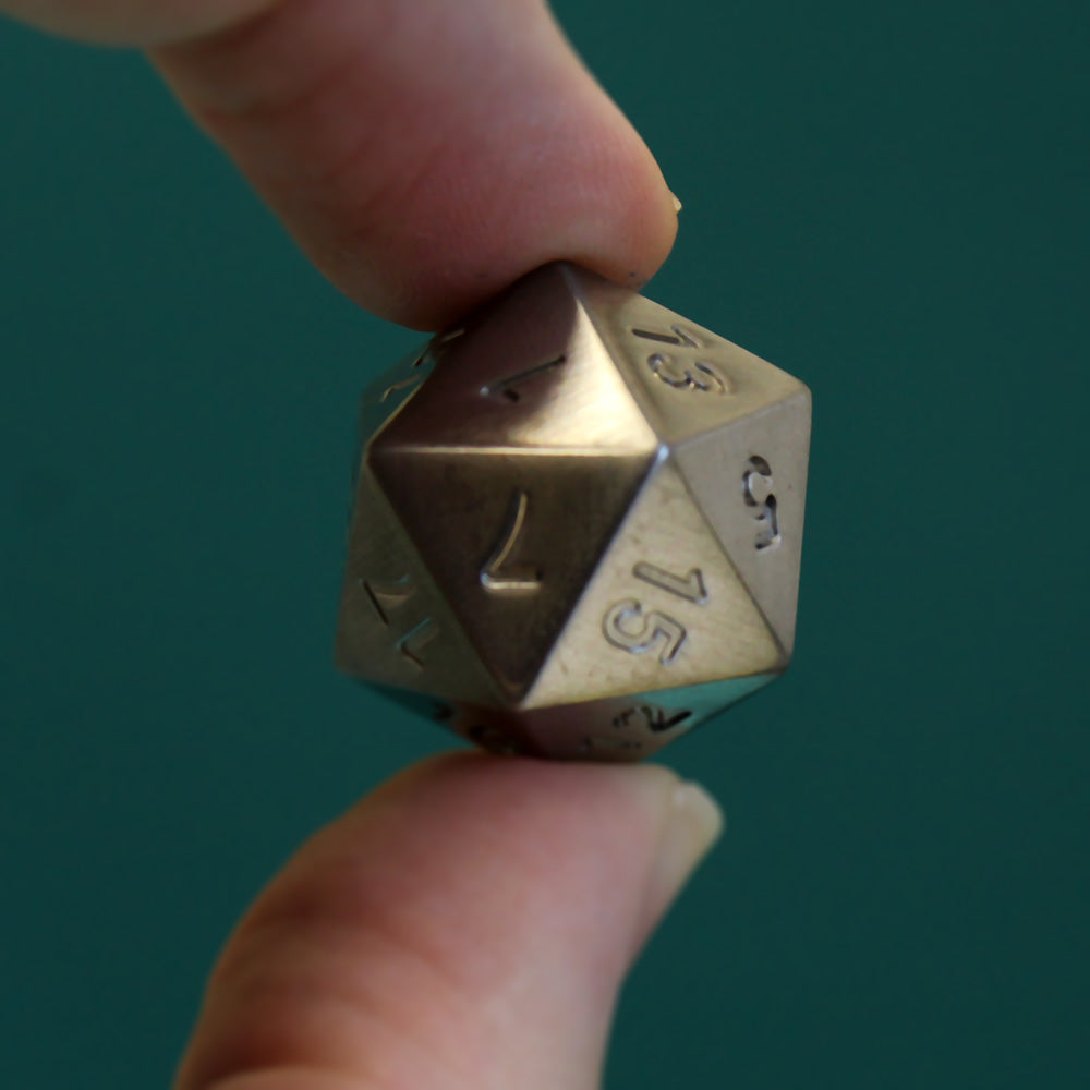Closeup of the 16mm tungsten d20 held by the thumb and forefinger for scale. Though smaller than the jumbo version, it is significantly heavier than your average polyhedral.