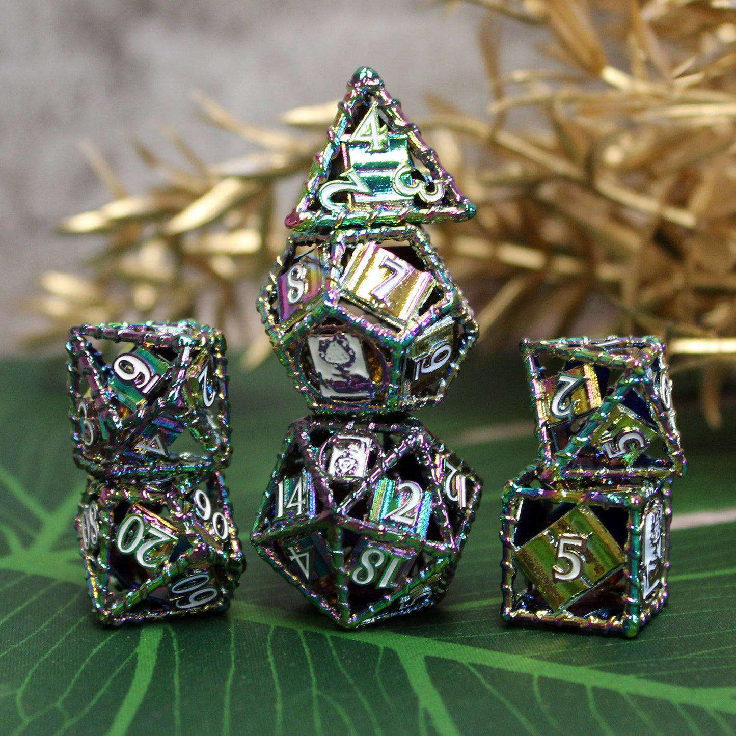 All 7 rainbow dice piled up in 3 stacks. Two dice in first stack, three dice in second stack, two dice in third stack. All on a green leaf surface with gold stems in background.