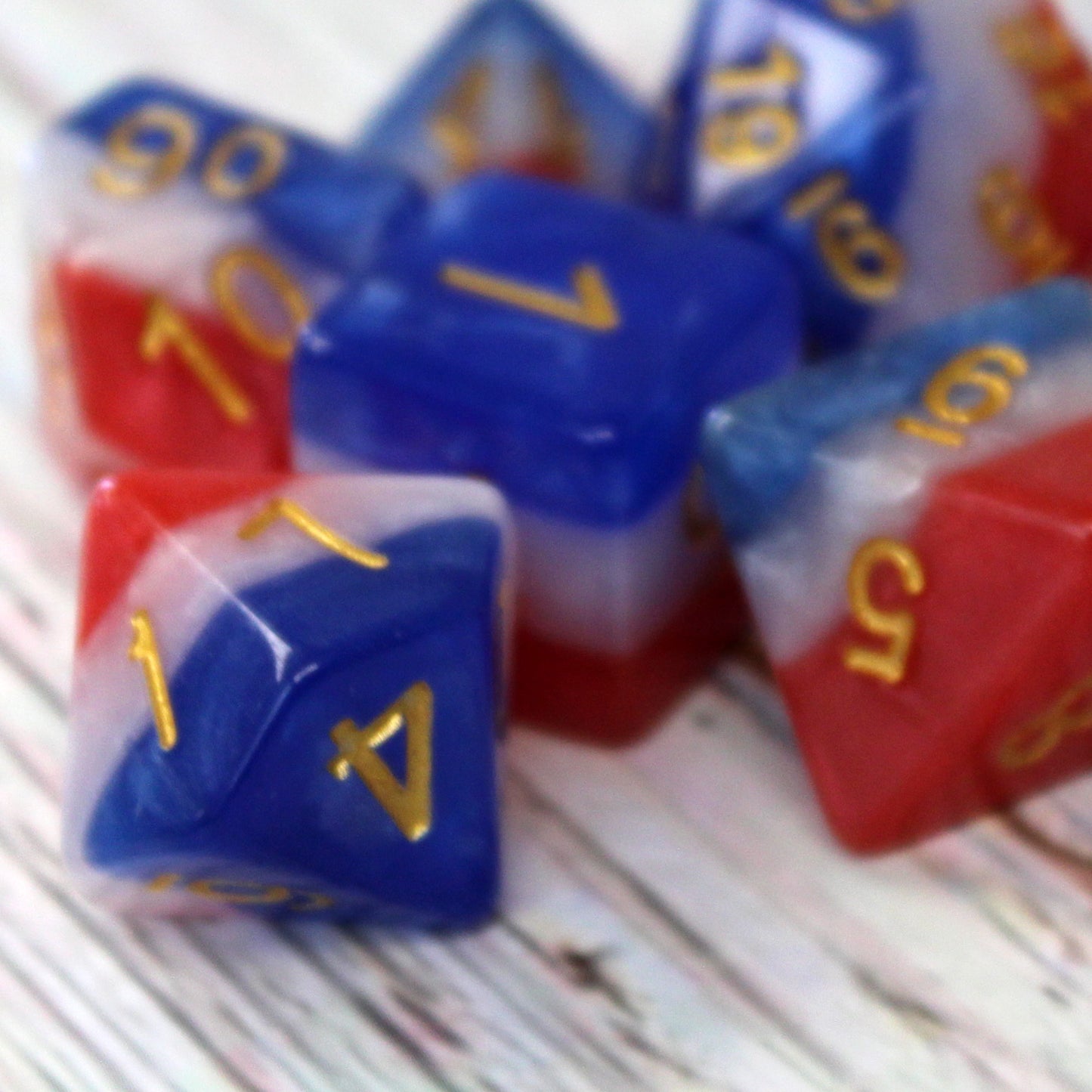 Close-up of a red, white, and blue layered dice set on a wooden table, showing the gold numbering clearly on each die face.