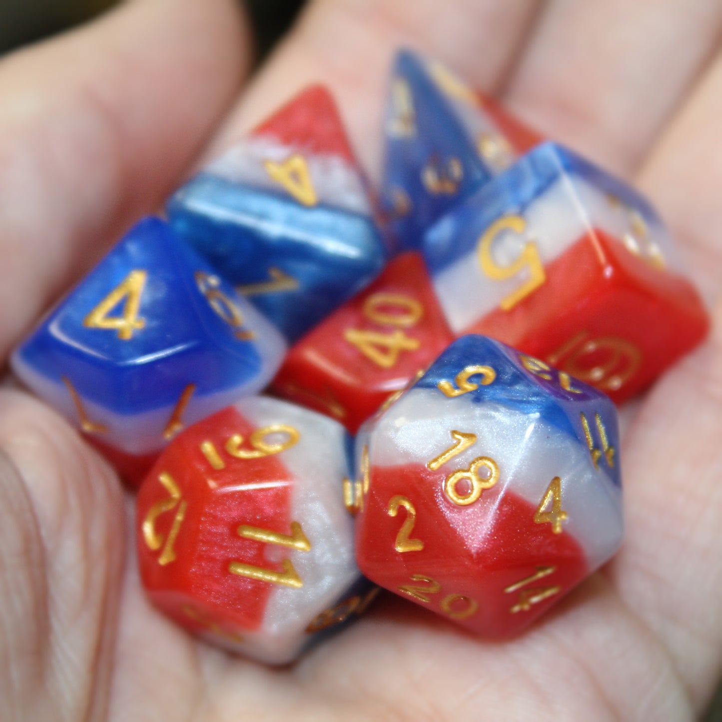 A hand holding the red, white, and blue layered dice set, with distinct layers of color and the easy-to-read gold numbering.