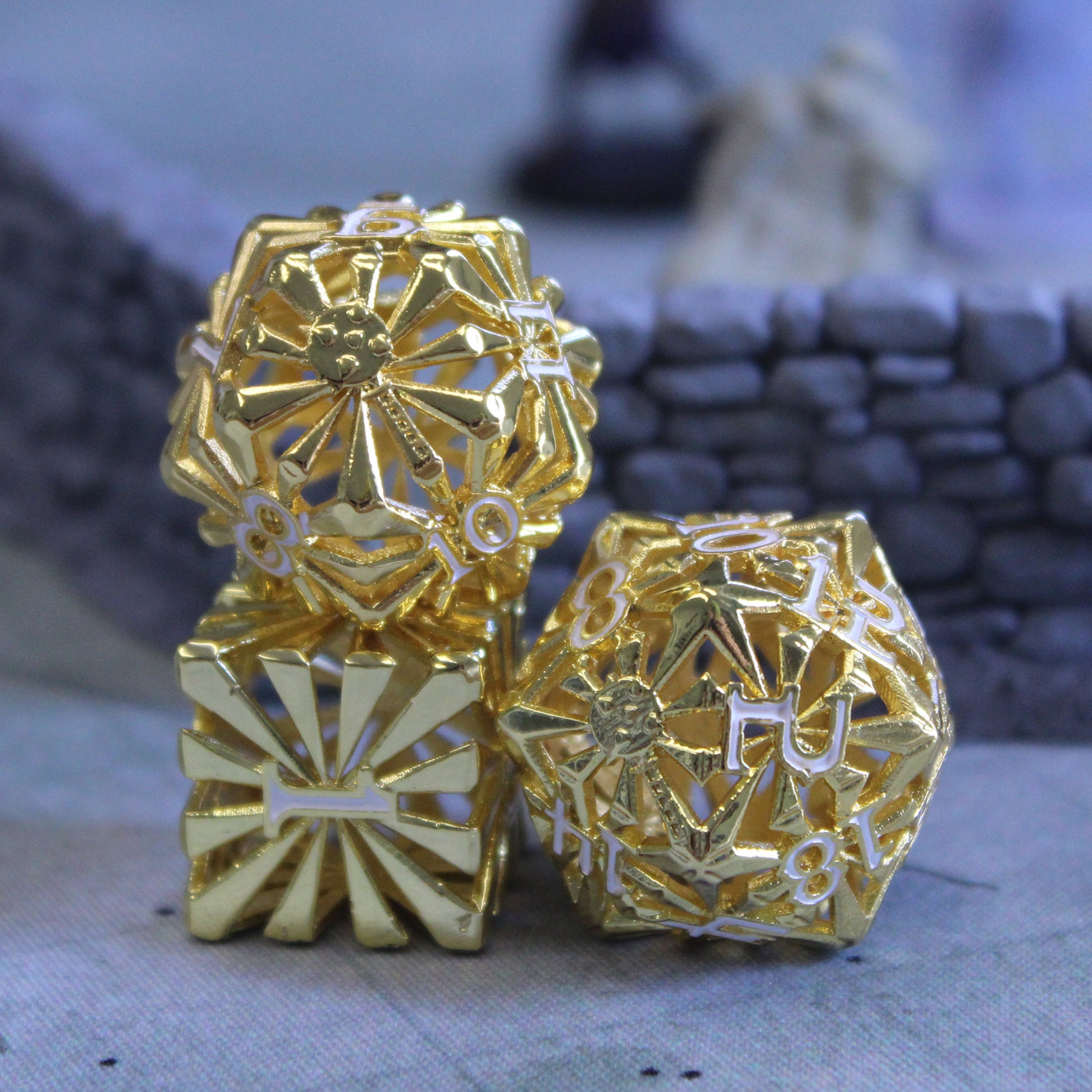 Closeup of bright gold-colored cleric-inspired hollow metal dice with white numbers and a mace in place of the high number on each die in play on a ttrpg battlefield