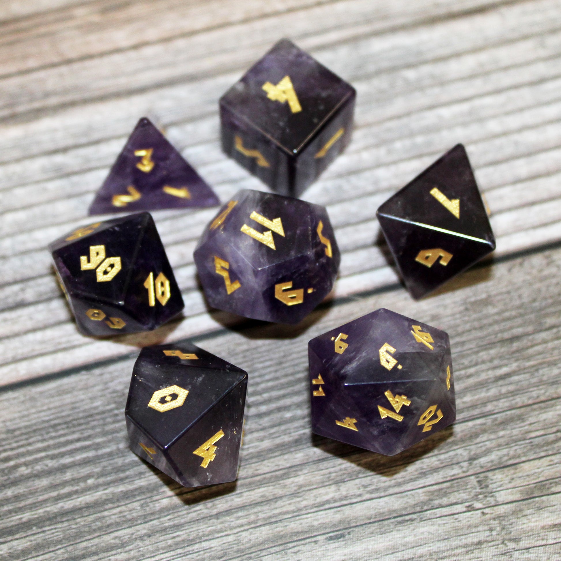 Amethyst gemstone dice arranged in a circle on a wooden table, shot from above to highlight the uniform precision cut and gold numbering.