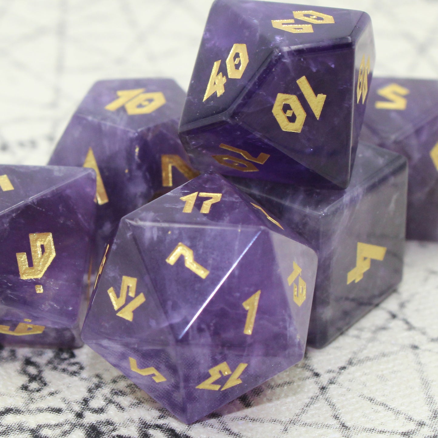 Close-up of Amethyst dice set on an antique map, highlighting the intricate gold numbering and natural lavender to indigo color variations.