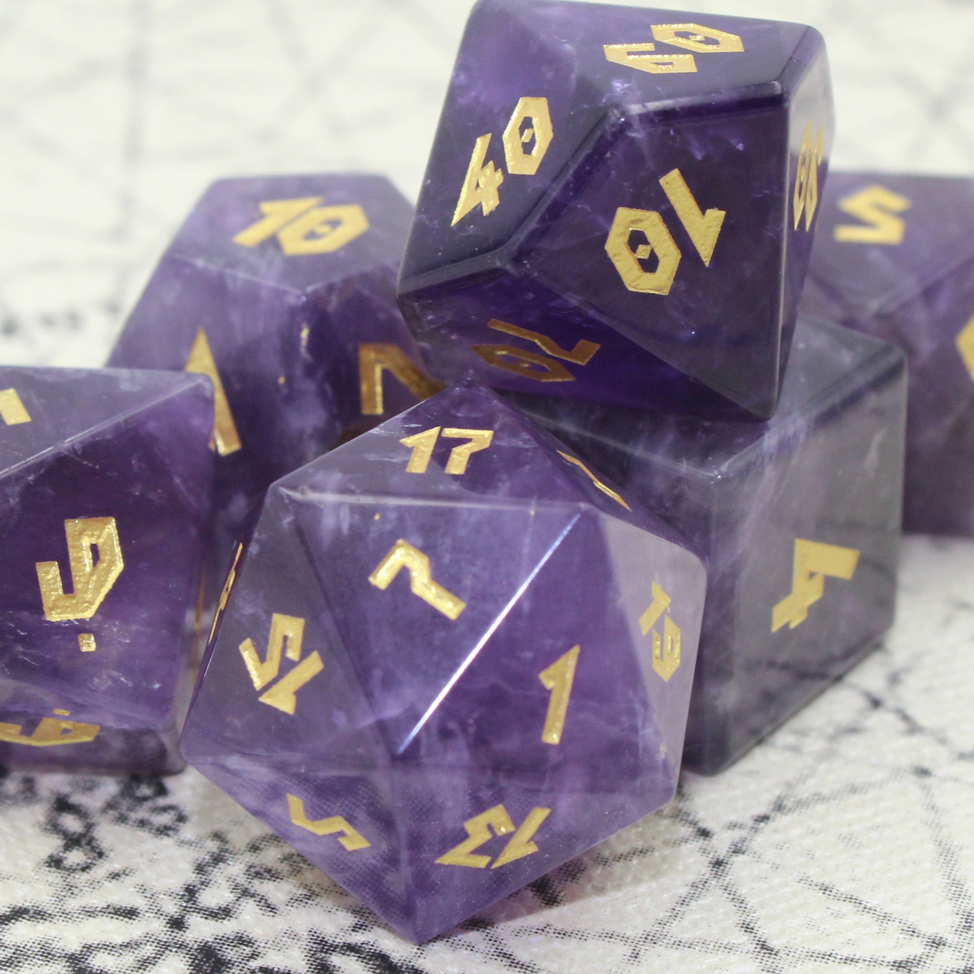Close-up of Amethyst dice set on an antique map, highlighting the intricate gold numbering and natural lavender to indigo color variations.