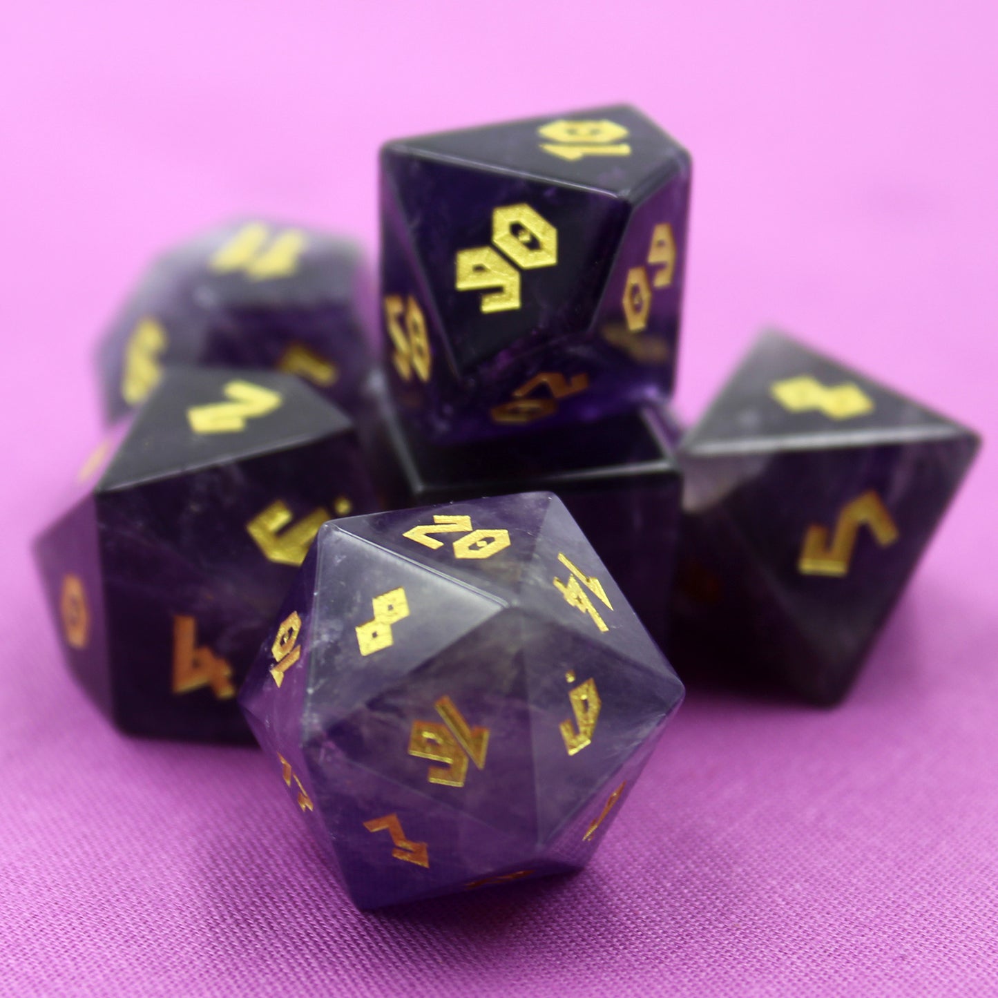 Full set of Amethyst gemstone dice displayed on a rich purple background, showcasing the violet hues and gold Roman font numbering.