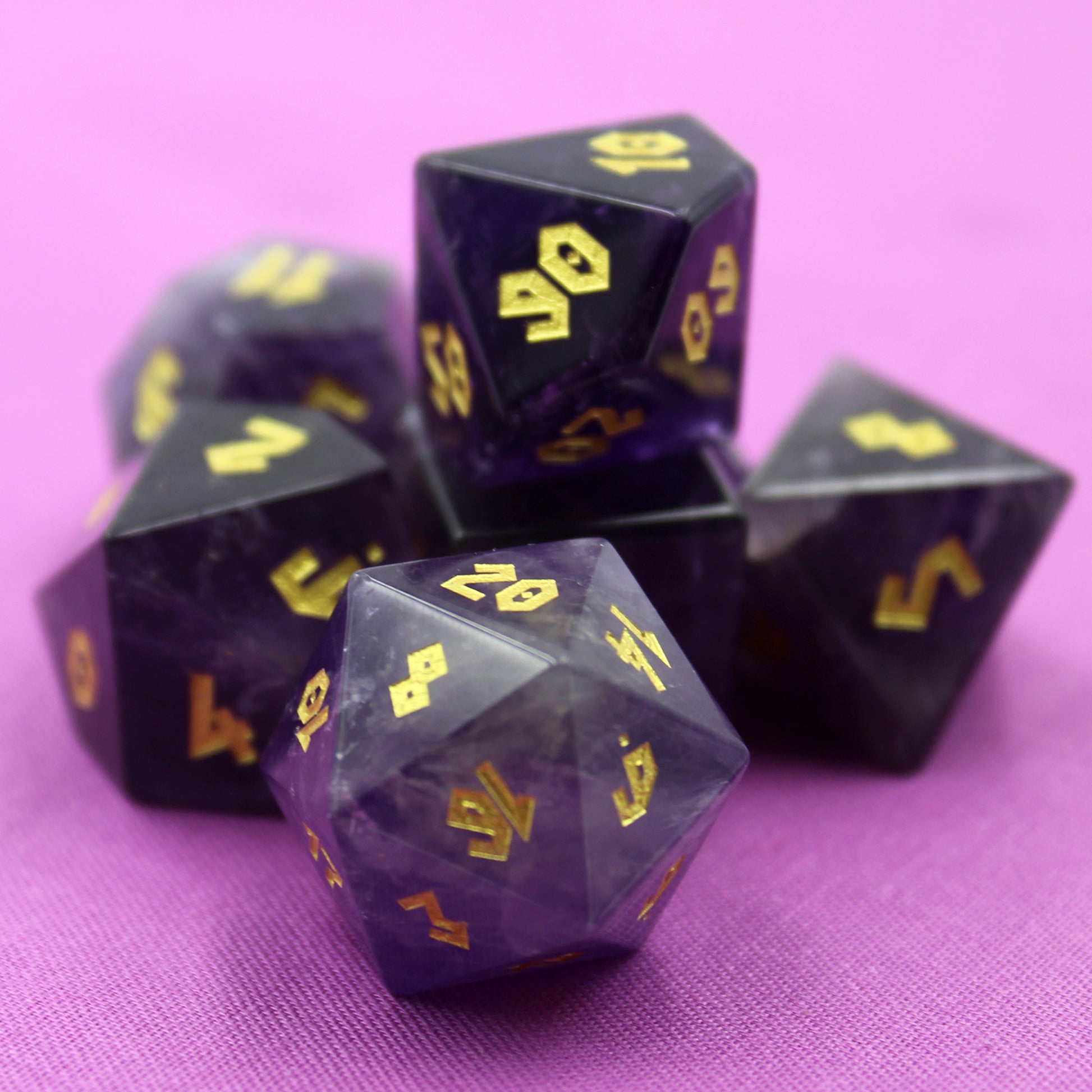 Full set of Amethyst gemstone dice displayed on a rich purple background, showcasing the violet hues and gold Roman font numbering.