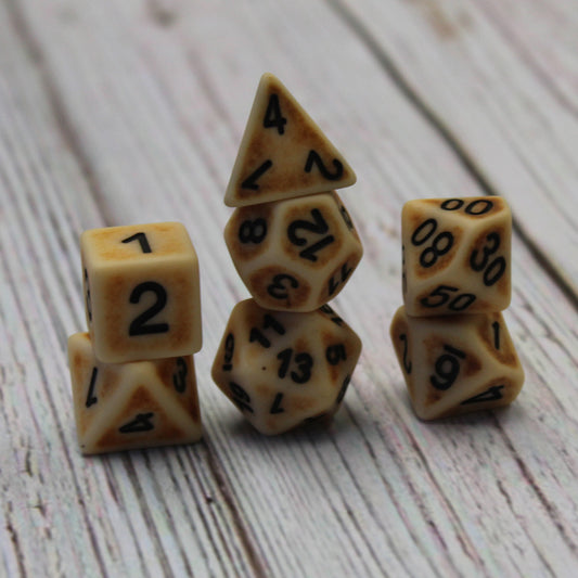 Ancient Bone Brown dice set in three stacks on a white wooden surface.