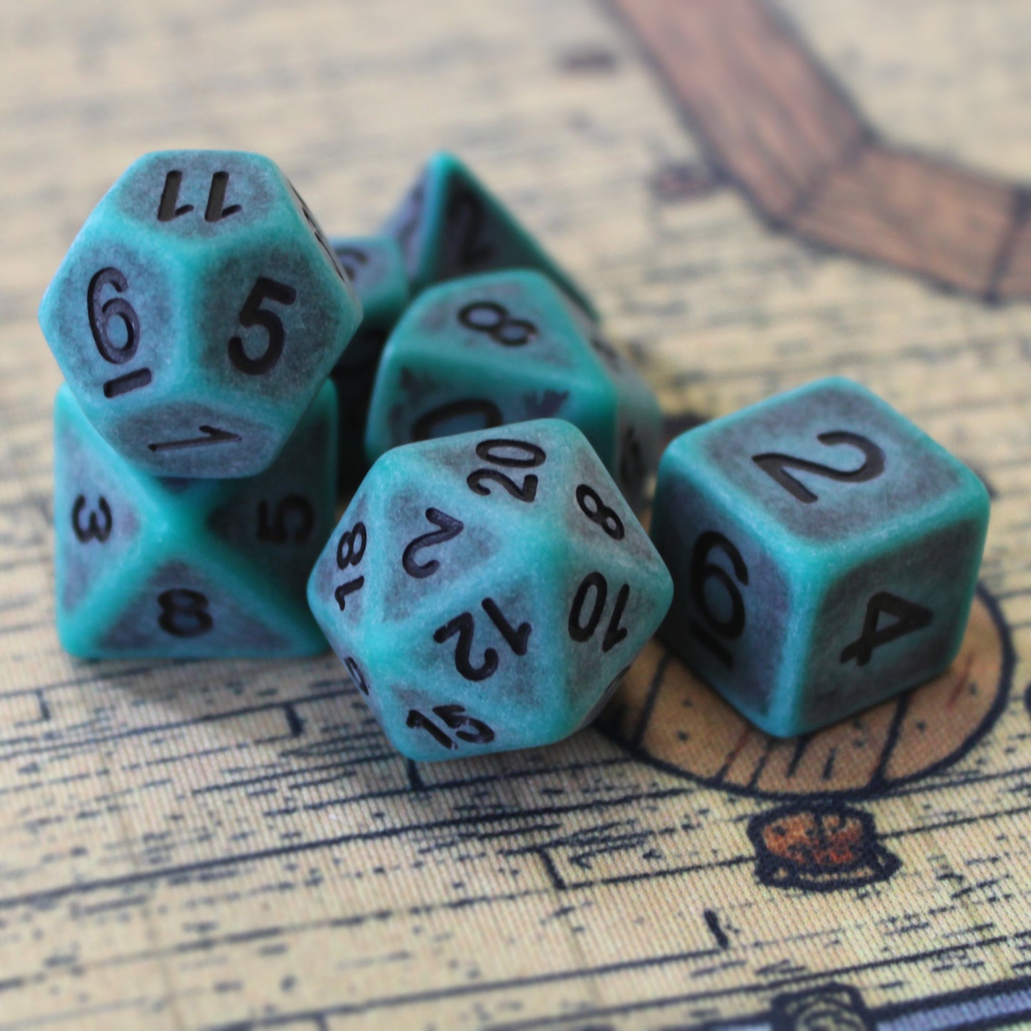 Closeup of a set of seven green plastic dice with black numbering designed to look aged on a playmat