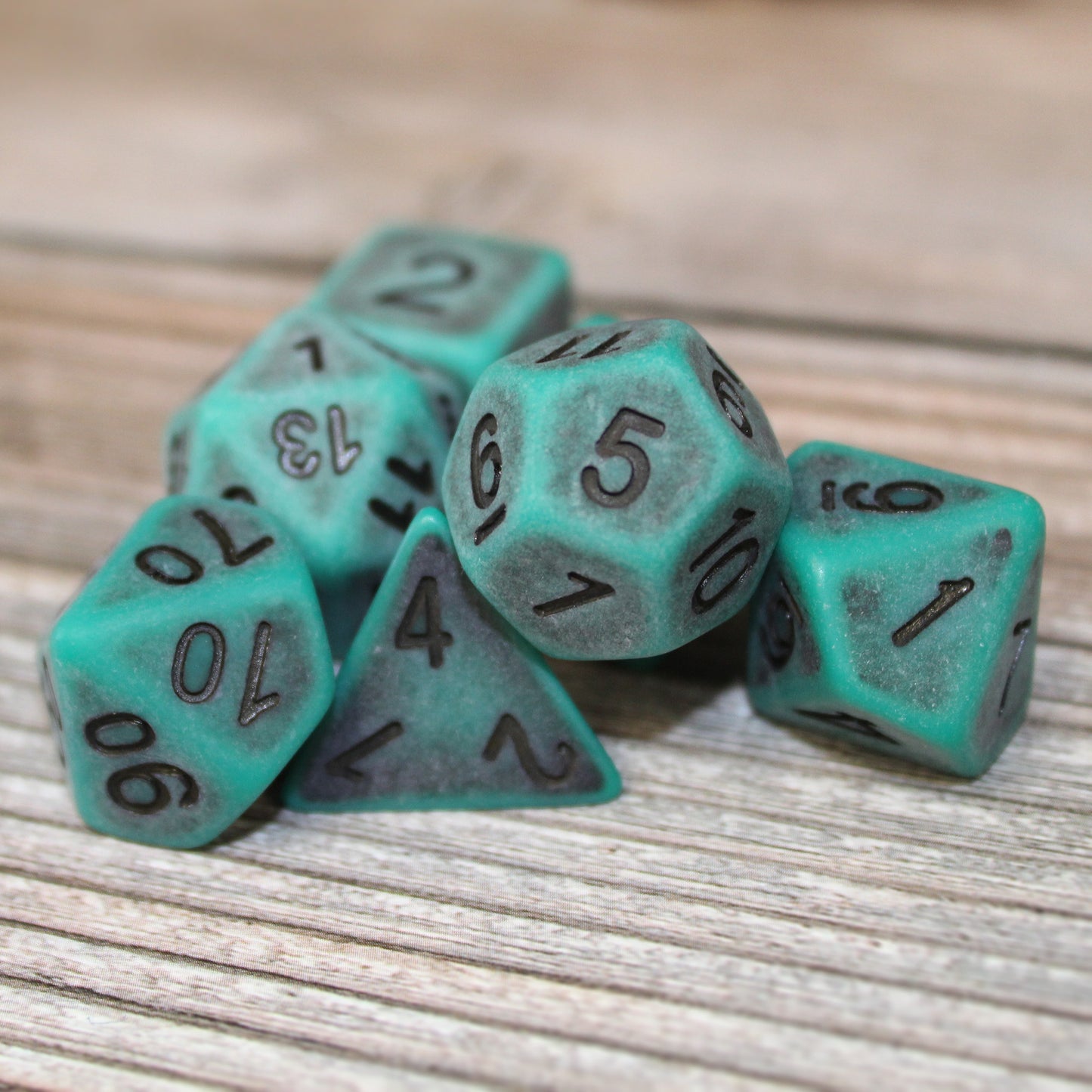 Closeup of a Set of seven green plastic dice with black numbering designed to look aged on a wooden background