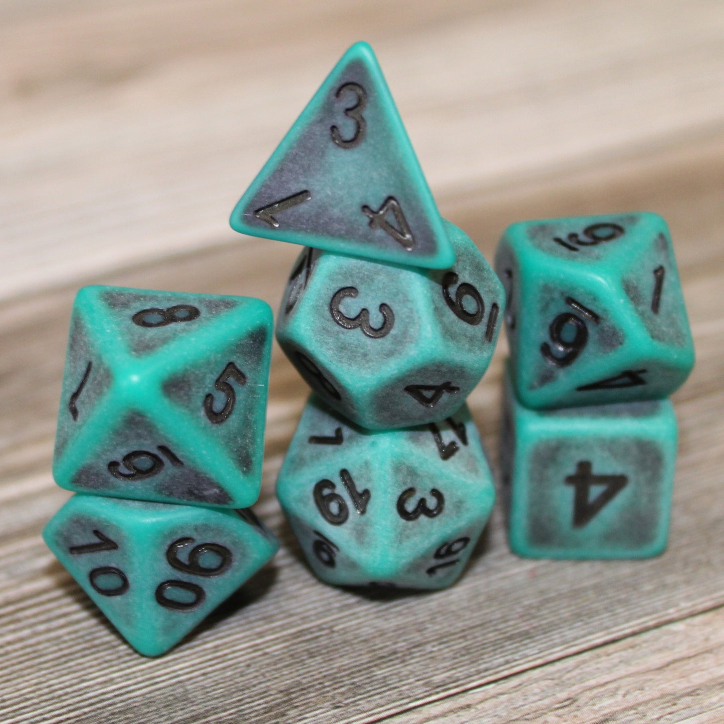 Closeup of a stacked set of seven green plastic dice with black numbering designed to look aged on a wooden background