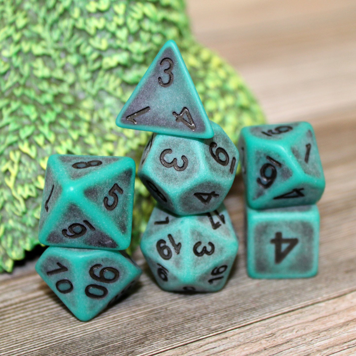 Closeup of a set of seven green plastic dice with black numbering designed to look aged on a play mat