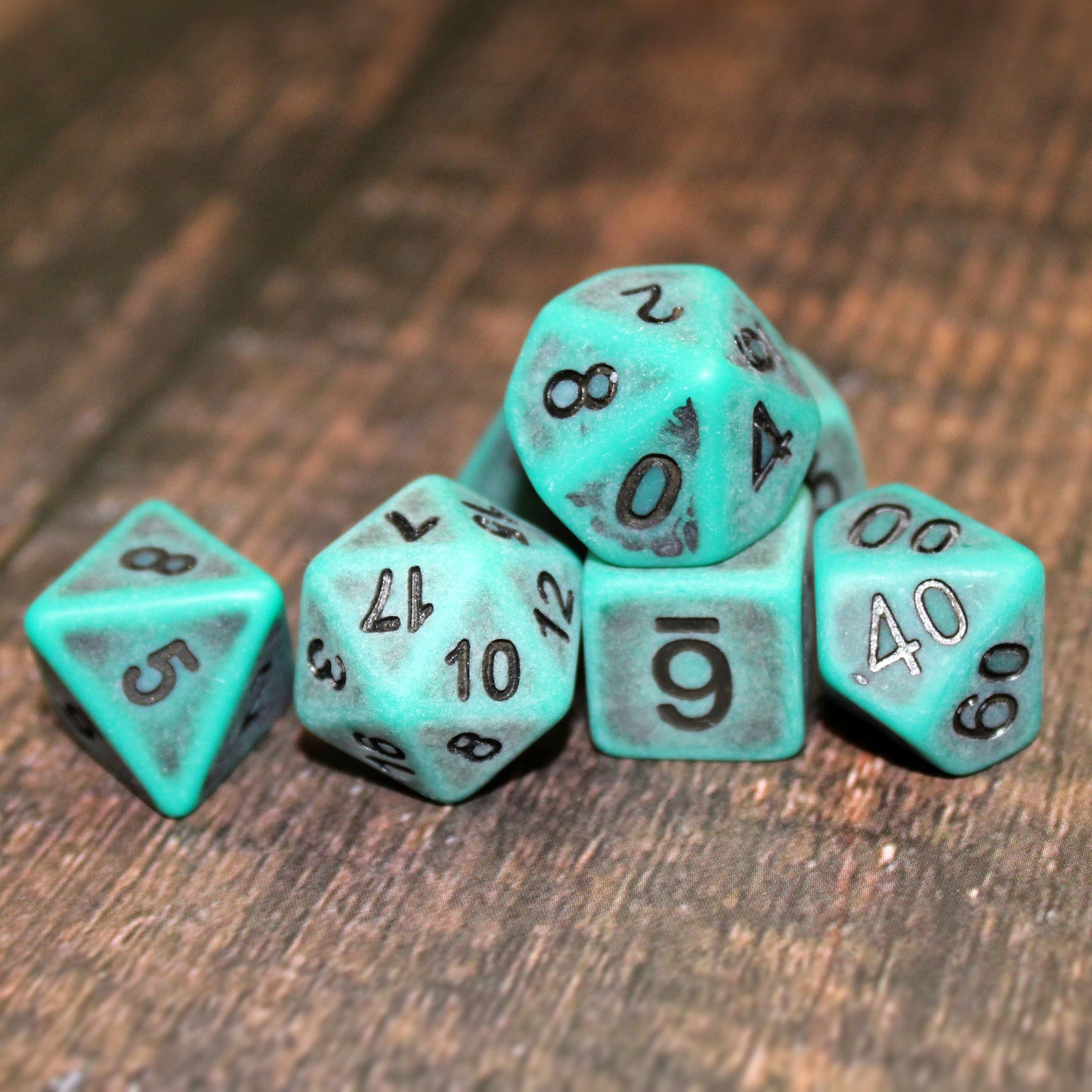 Set of seven green plastic dice with black numbering designed to look aged on a wooden background