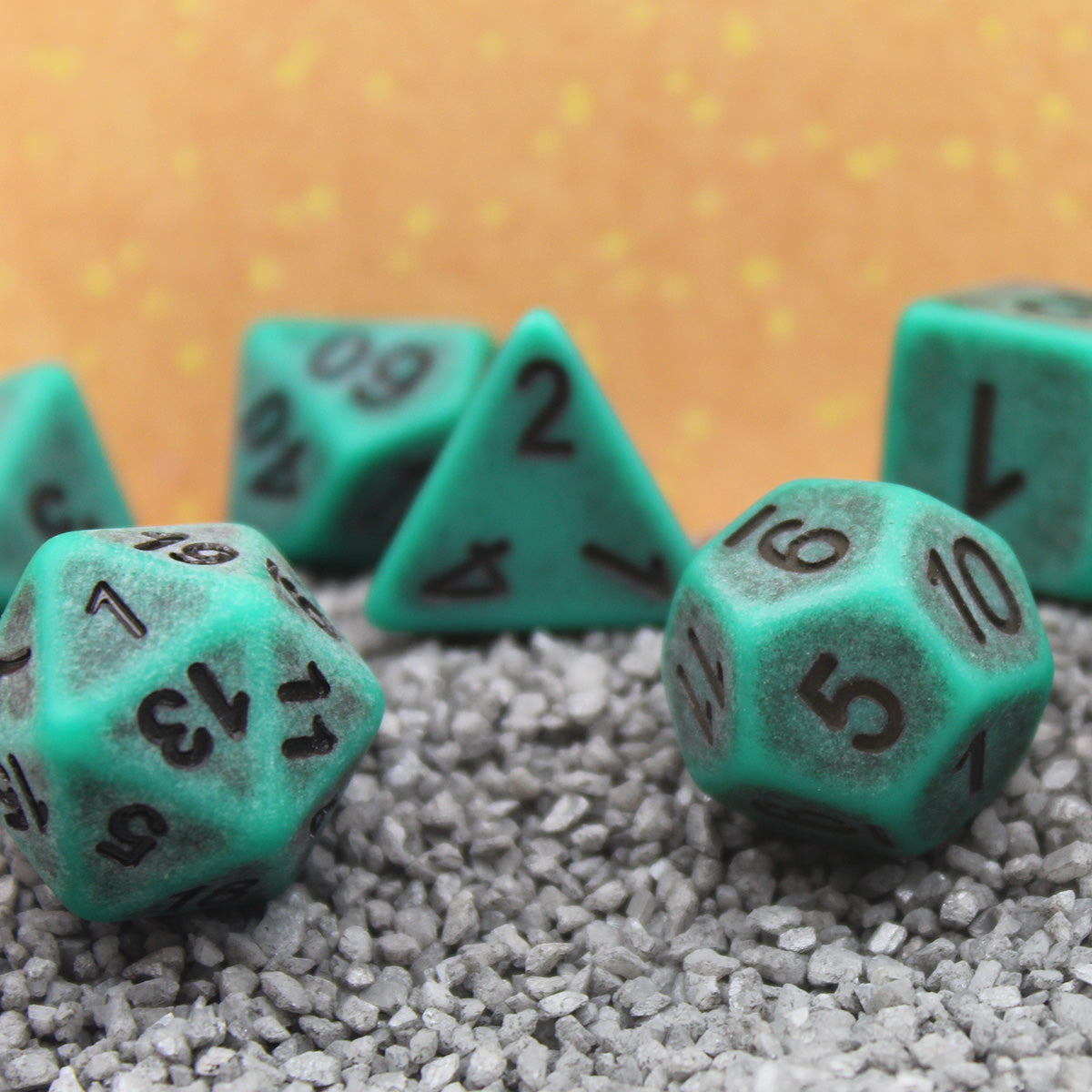 Closeup of a Set of seven green plastic dice with black numbering designed to look aged on a bed of gravel