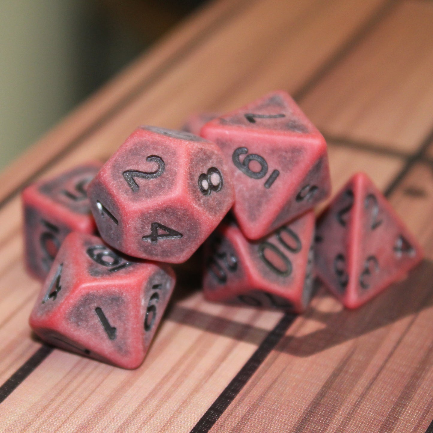 Weathered dust crimson dice set with deep-carved black numbering, showcasing its rugged texture, perfect for tabletop RPGs like Dungeons & Dragons or Pathfinder.