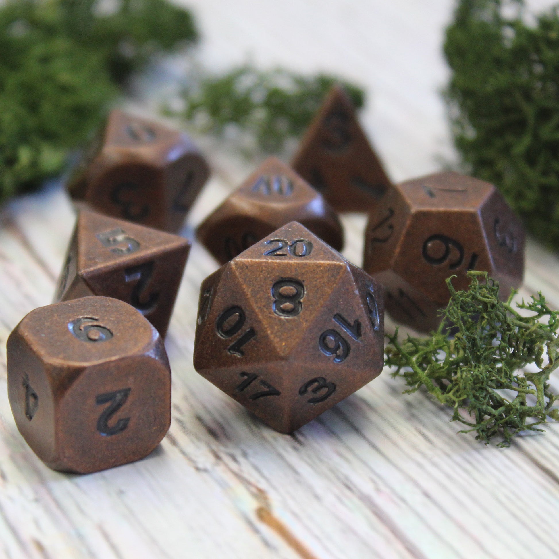 Primordial Copper dice set arranged on a light wooden surface, surrounded by green foliage.