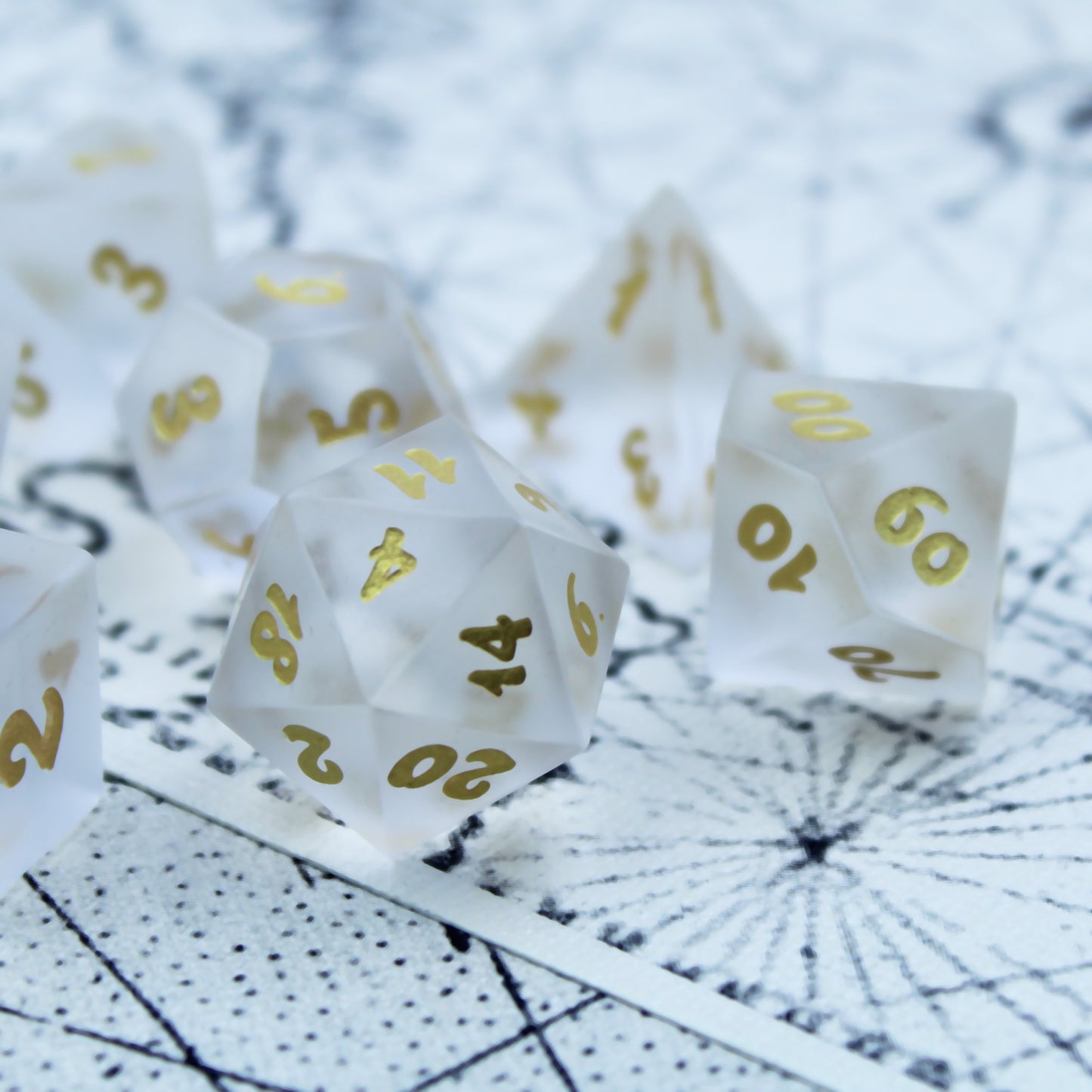 Closeup of a set of white frosted glass RPG dice with golden font on a black and white patterned mat