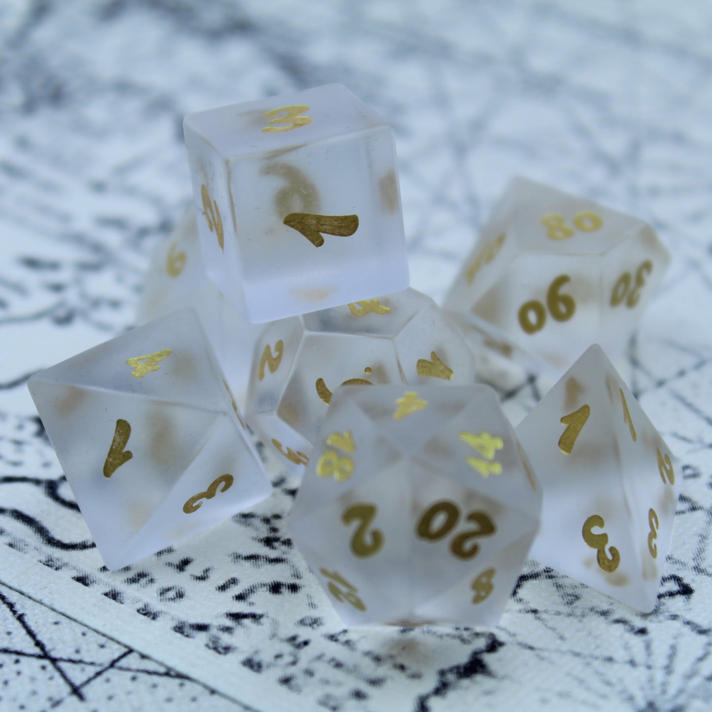 Set of white frosted glass RPG dice with golden font sitting on a patterned white and black mat