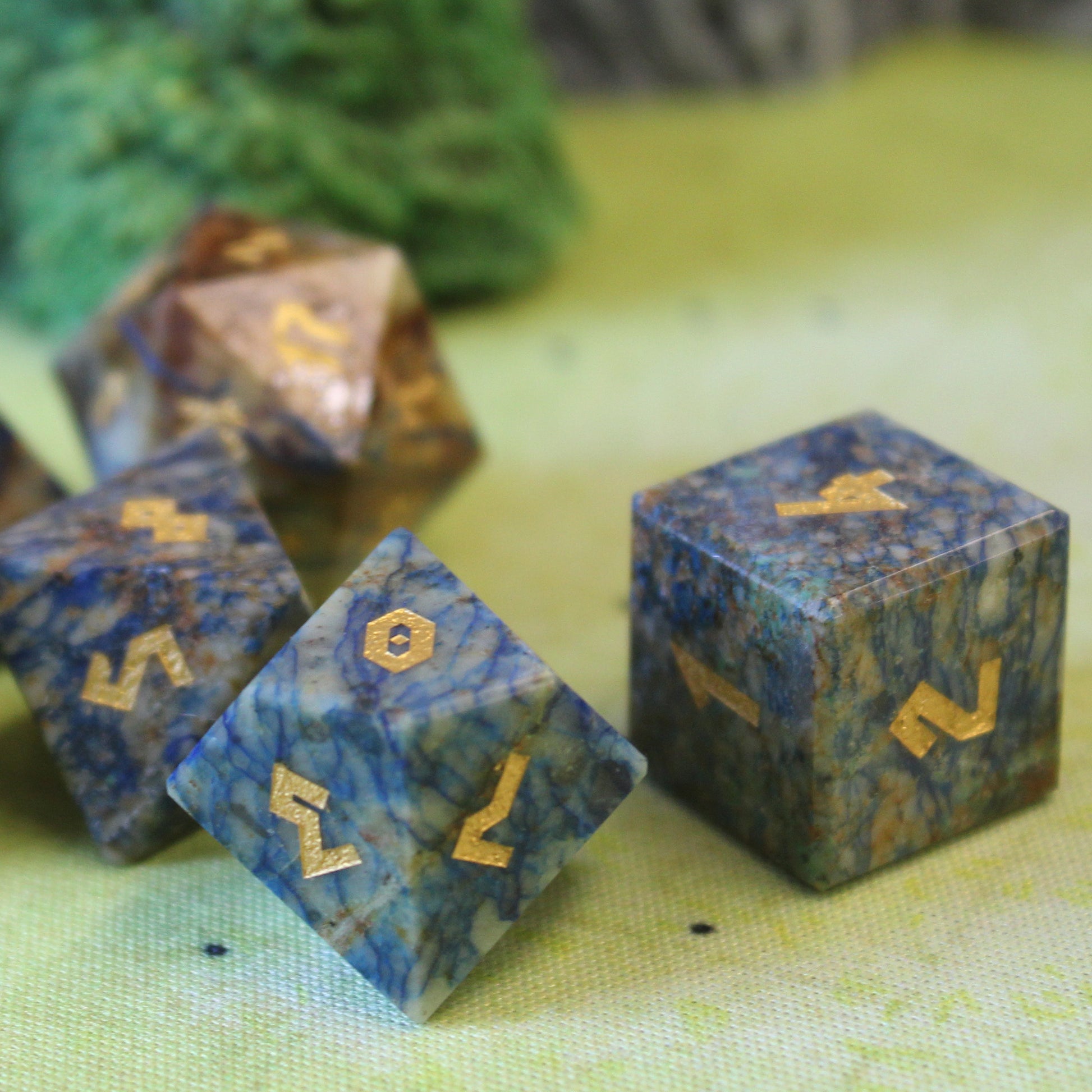 Close-up of four of the Azurite dice on a green play mat, with a foliage set piece behind them.