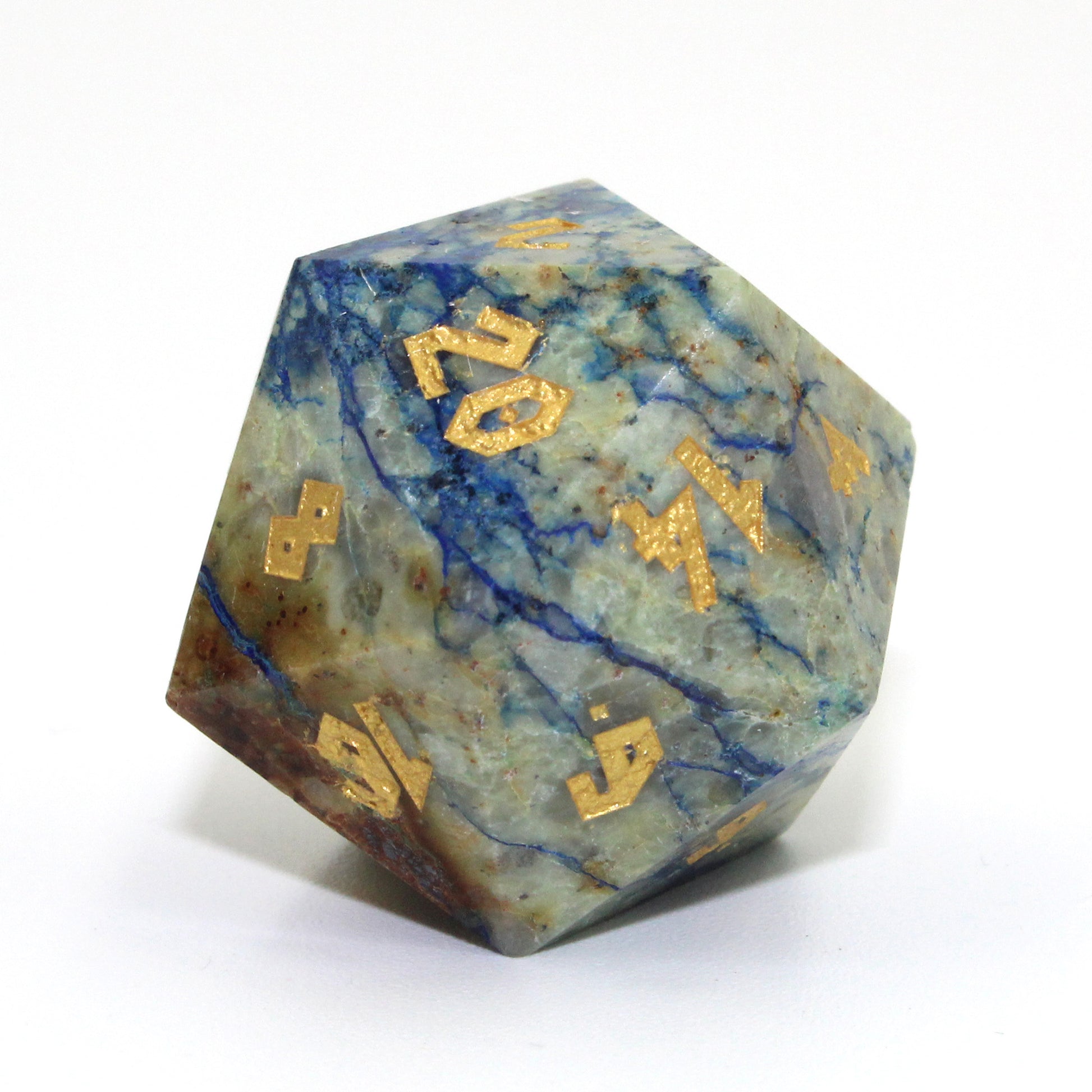 Close-up of the Azurite D20 die on a white background. The veins of blue and green can be seen through the mineral, with gold numbering on each face.