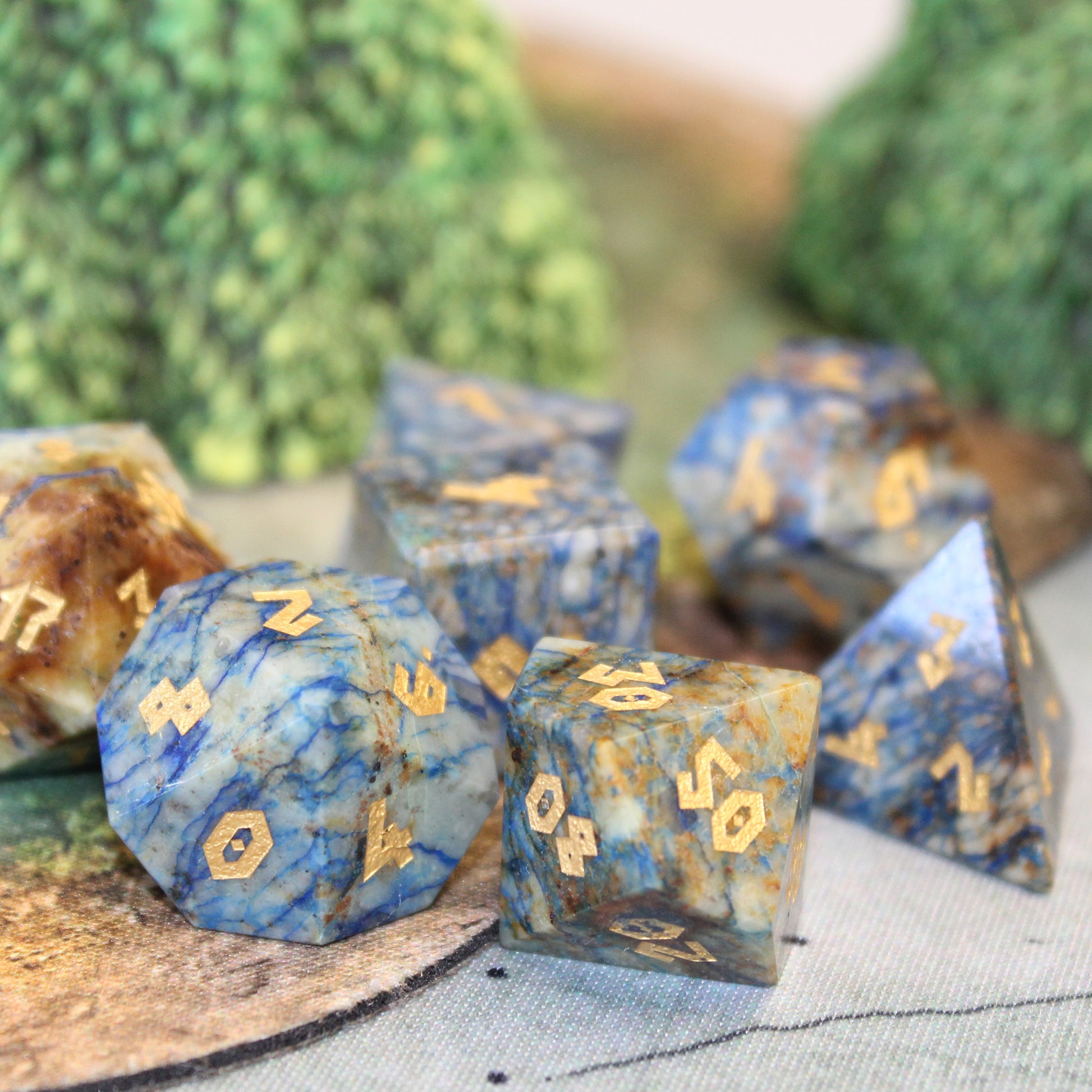Azurite dice set scattered on a play mat, with foliage set pieces behind them.