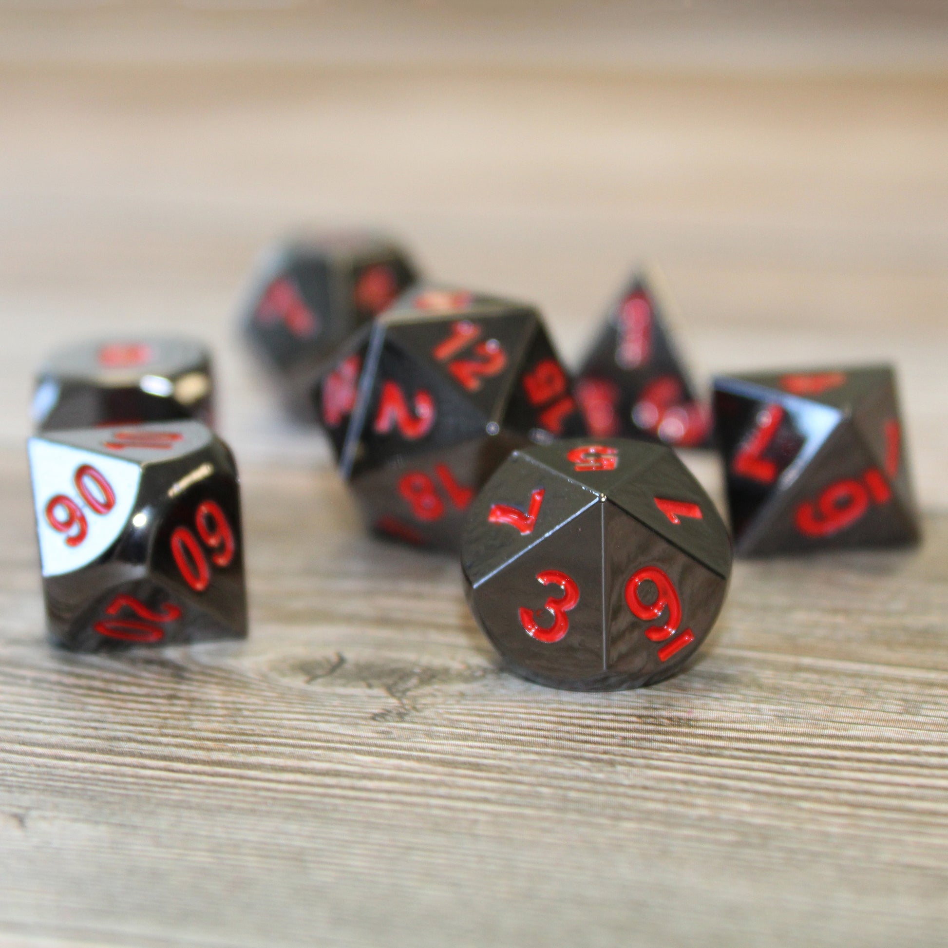 Metal Black Ember dice set scattered on top of a light colored wood surface