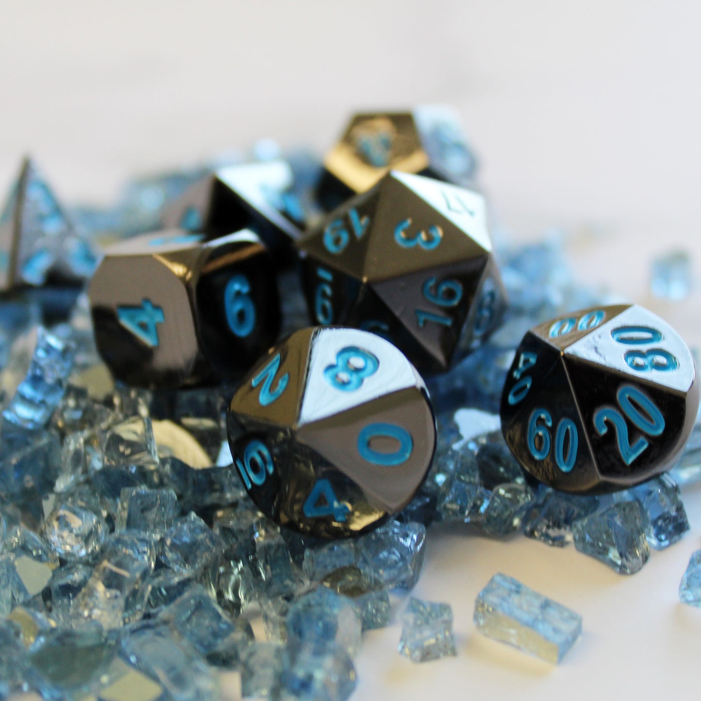 Metal Black Frost Dice Set scattered on top of light blue glass shards on a white background