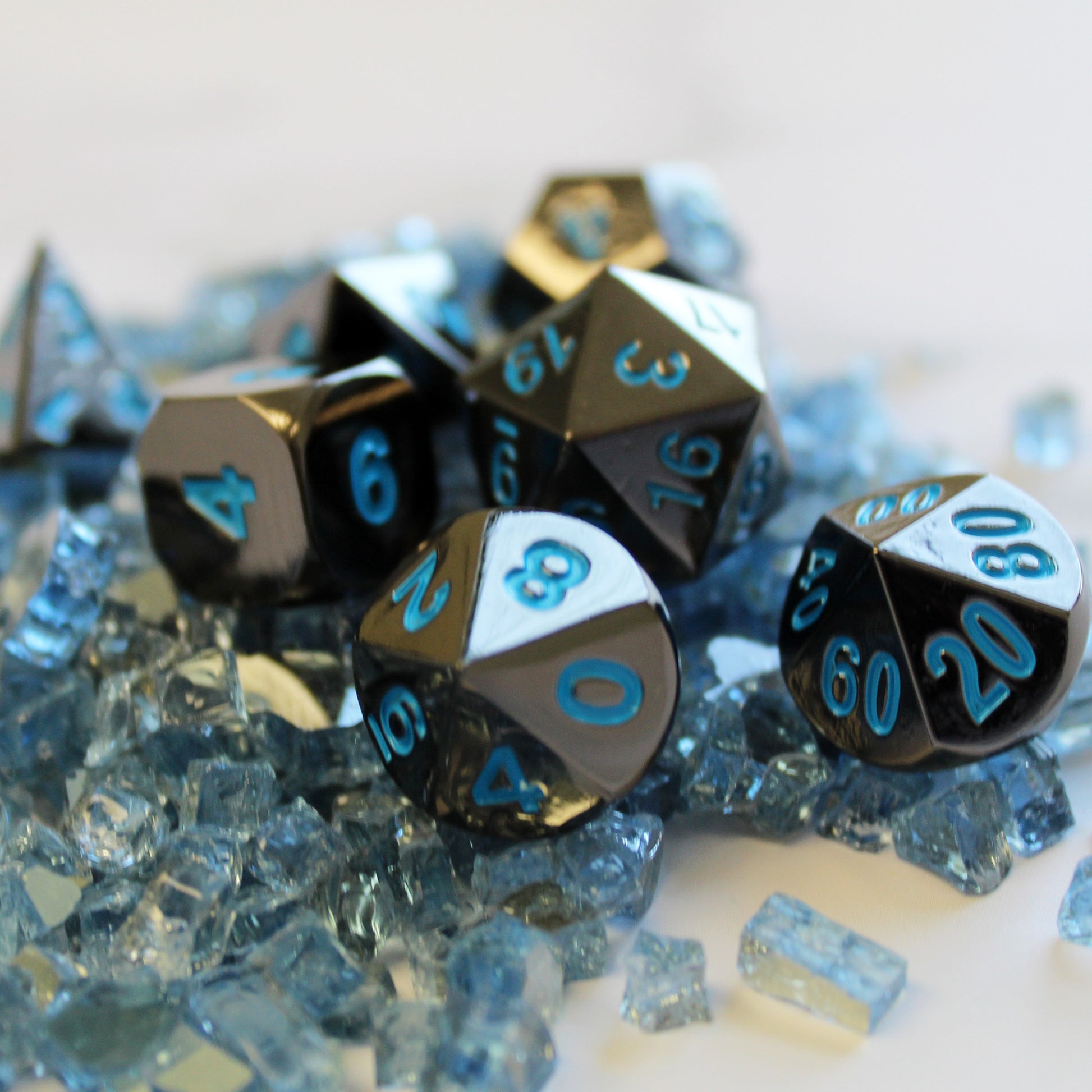 Metal Black Frost Dice Set scattered on top of light blue glass shards on a white background
